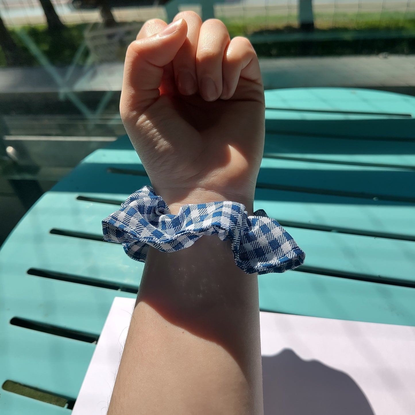 A blue gingham scrunchie modelled on a wrist.