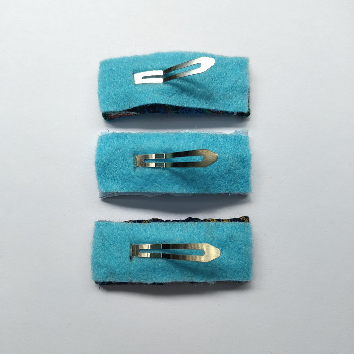 Three rectangular hair clips upside down displaying blue felt underneath and a silver prong.