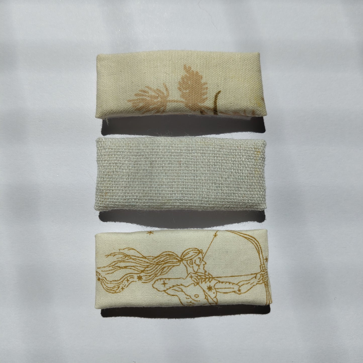 A trio of rectangular cream hair clips; floral, plain and astrology, on a plain white background.