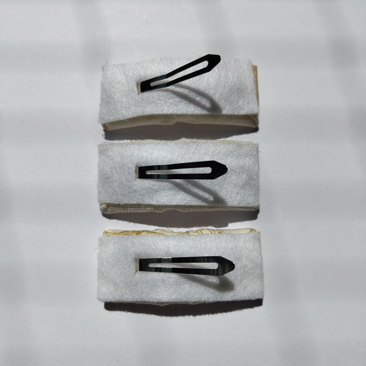 Three rectangular hair clips upside down displaying white felt underneath and a silver prong.