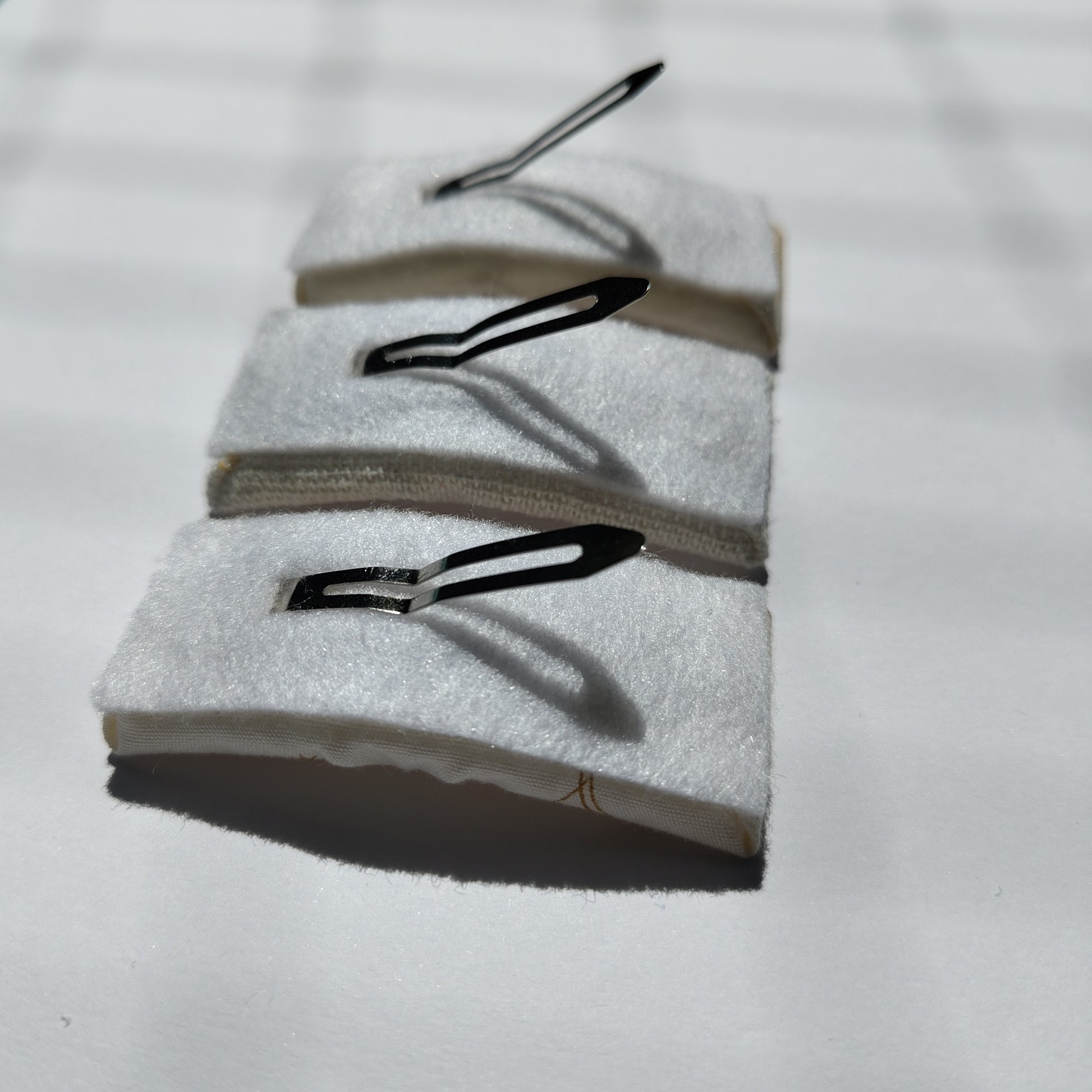 Three rectangular hair clips upside down displaying white felt underneath and a silver prong.