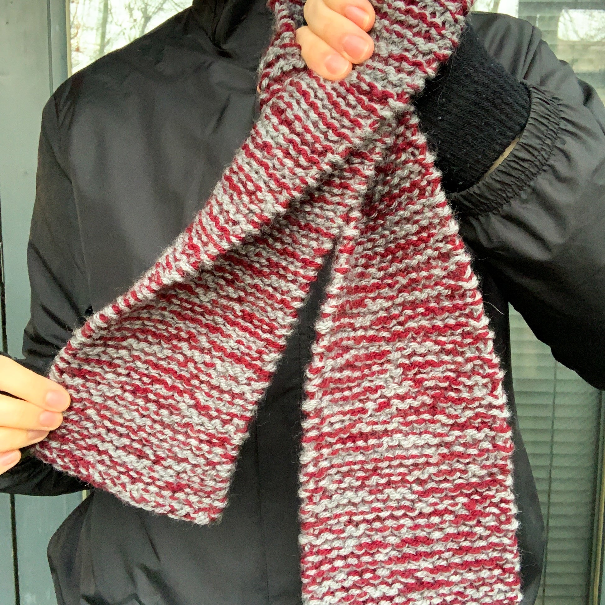 A burgundy and grey variegated scarf in held up a displayed by a person