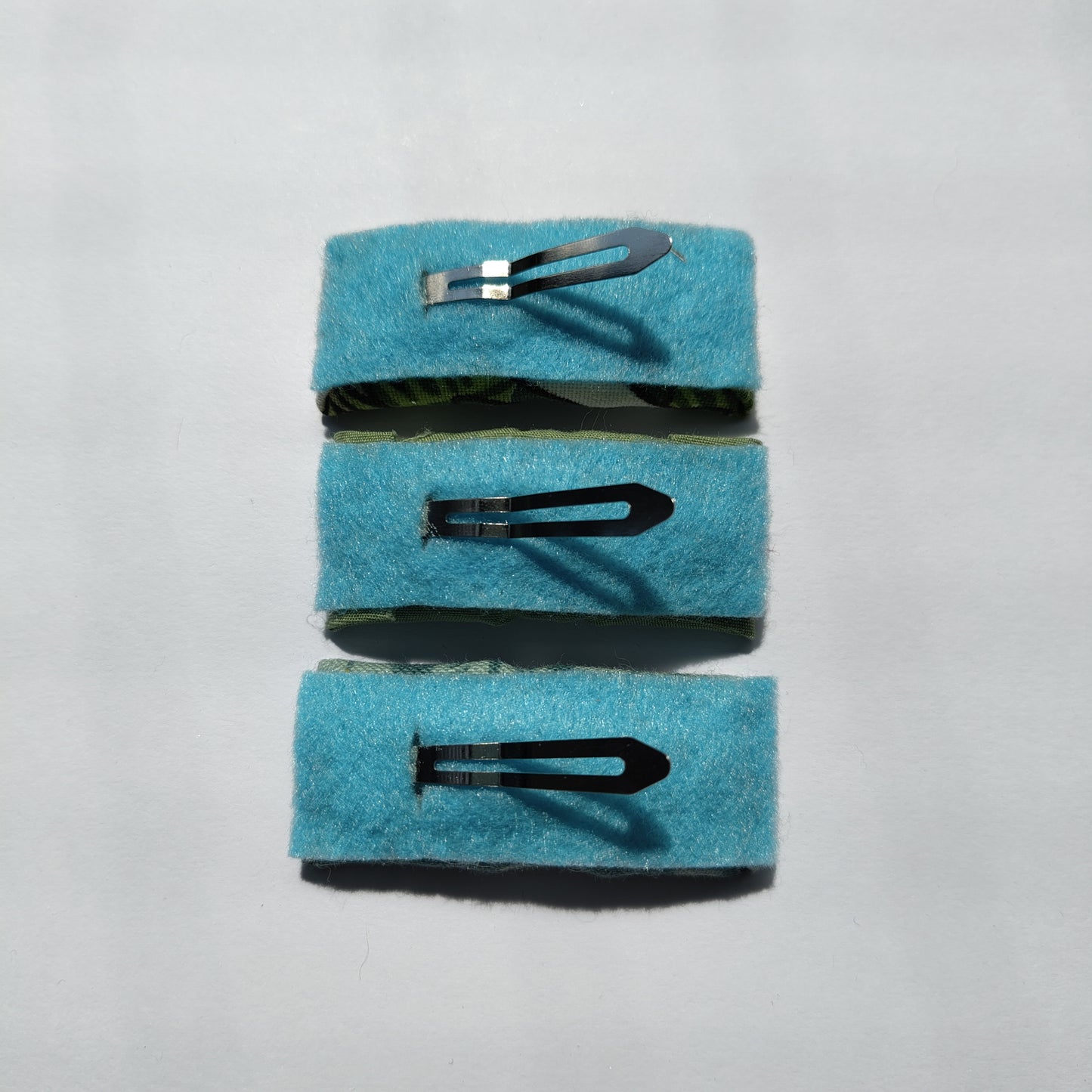 Three rectangular hair clips upside down displaying blue felt underneath and a silver prong.