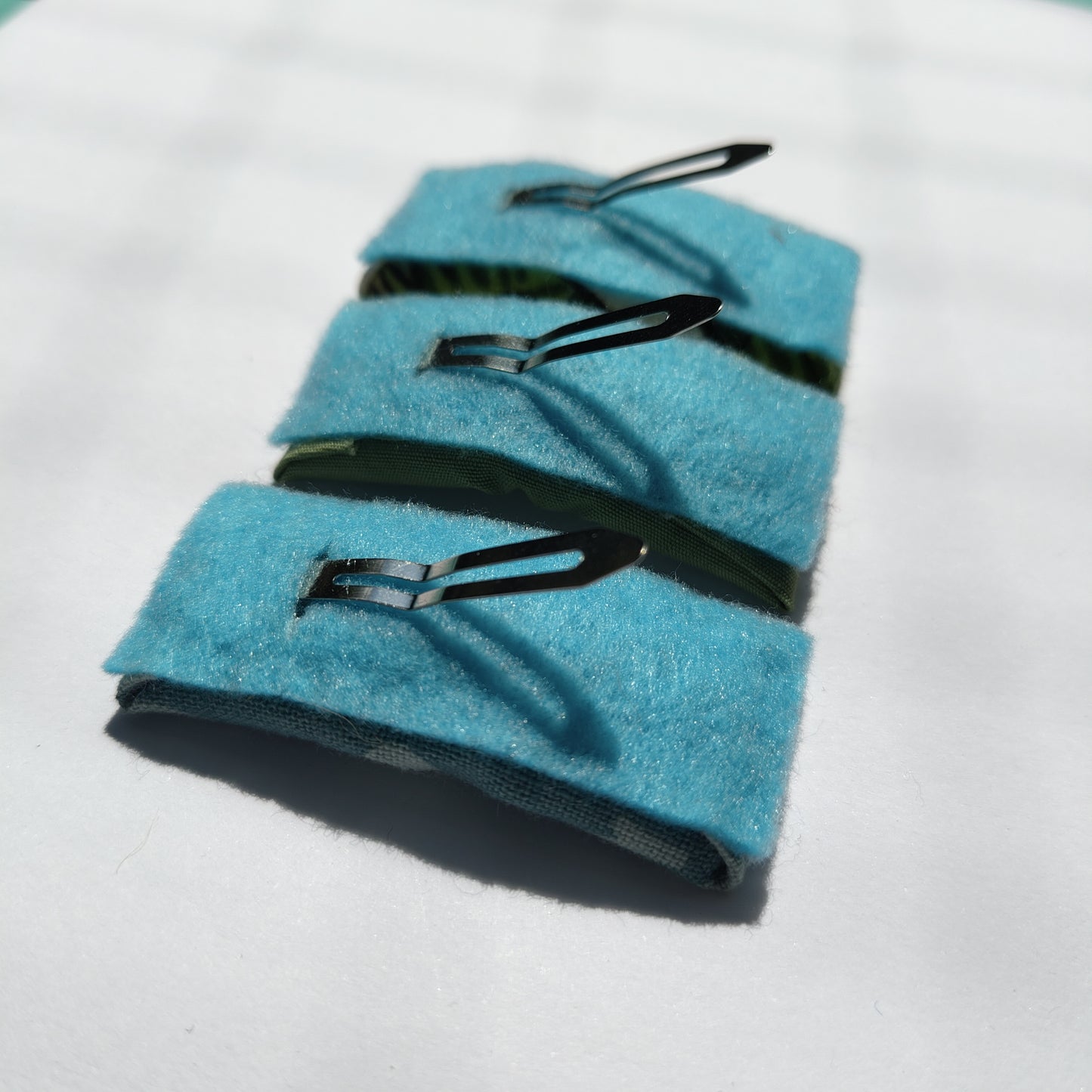 Three rectangular hair clips upside down displaying blue felt underneath and a silver prong.