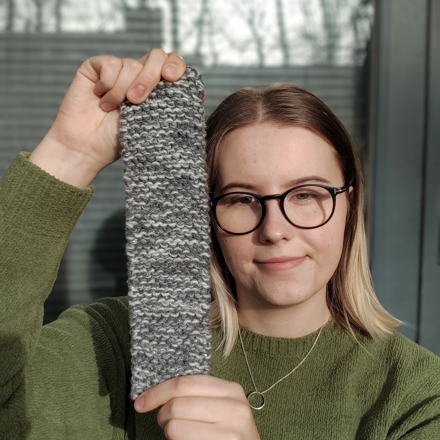 A woman holds up a beige variegated ear warmer knitted headband