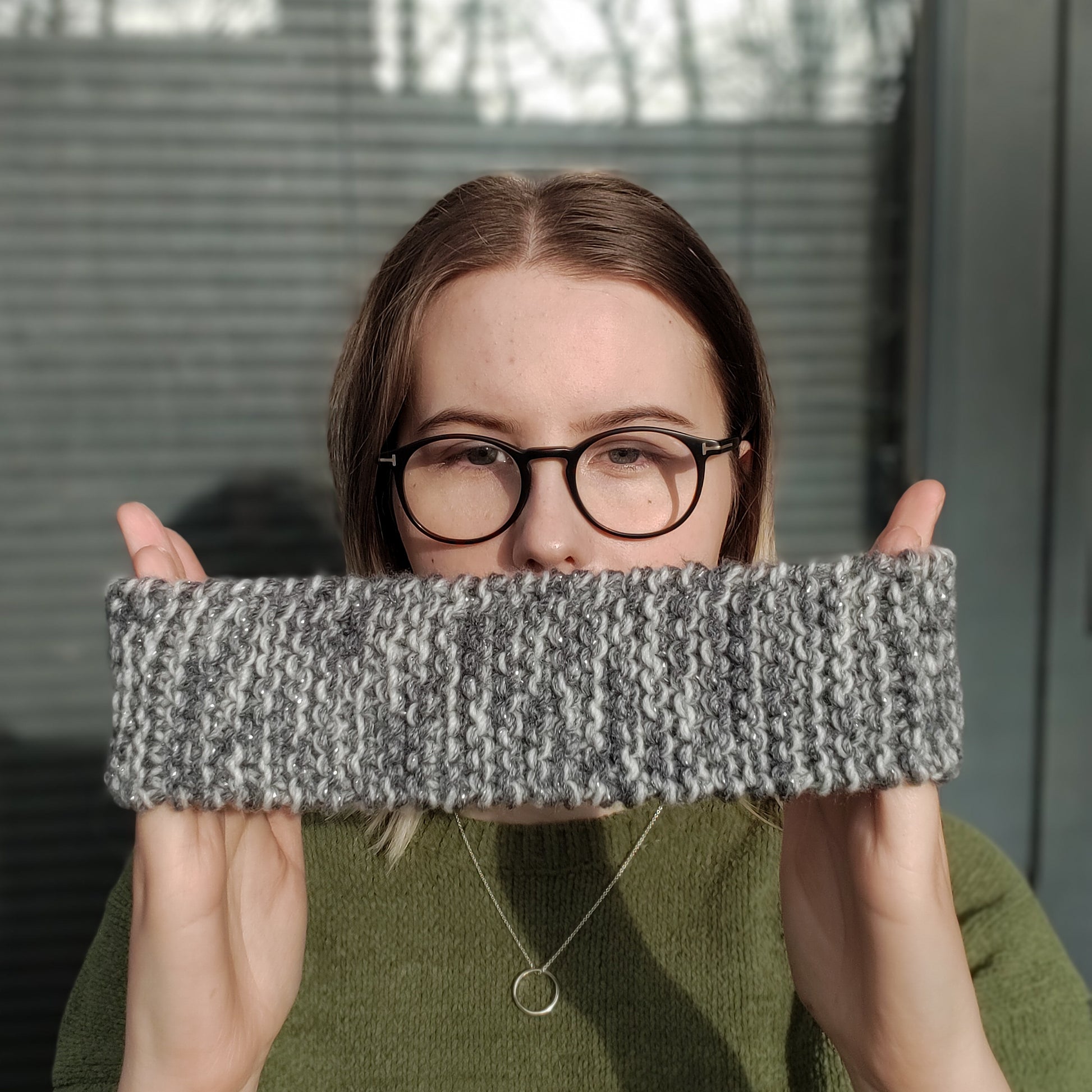 A woman holds a beige variegated ear warmer knitted headband between her hands