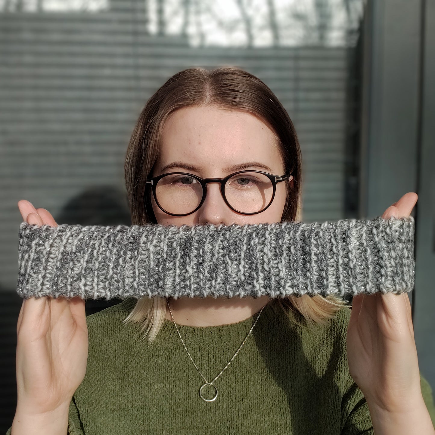 A woman holds a beige variegated ear warmer knitted headband stretched between her hands