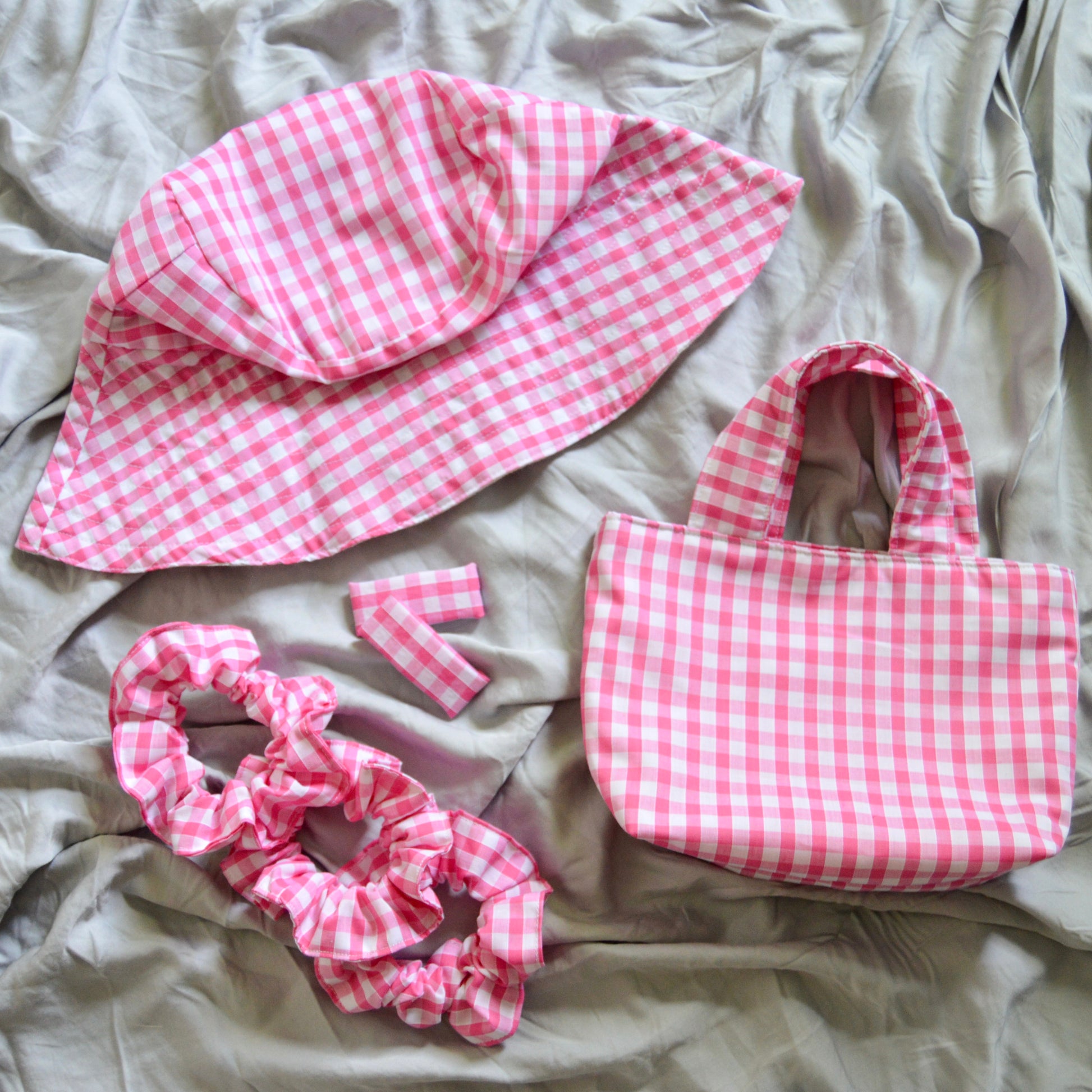 A bright pink gingham bucket sun hat lays with matching scrunchies tote bag and hair clips