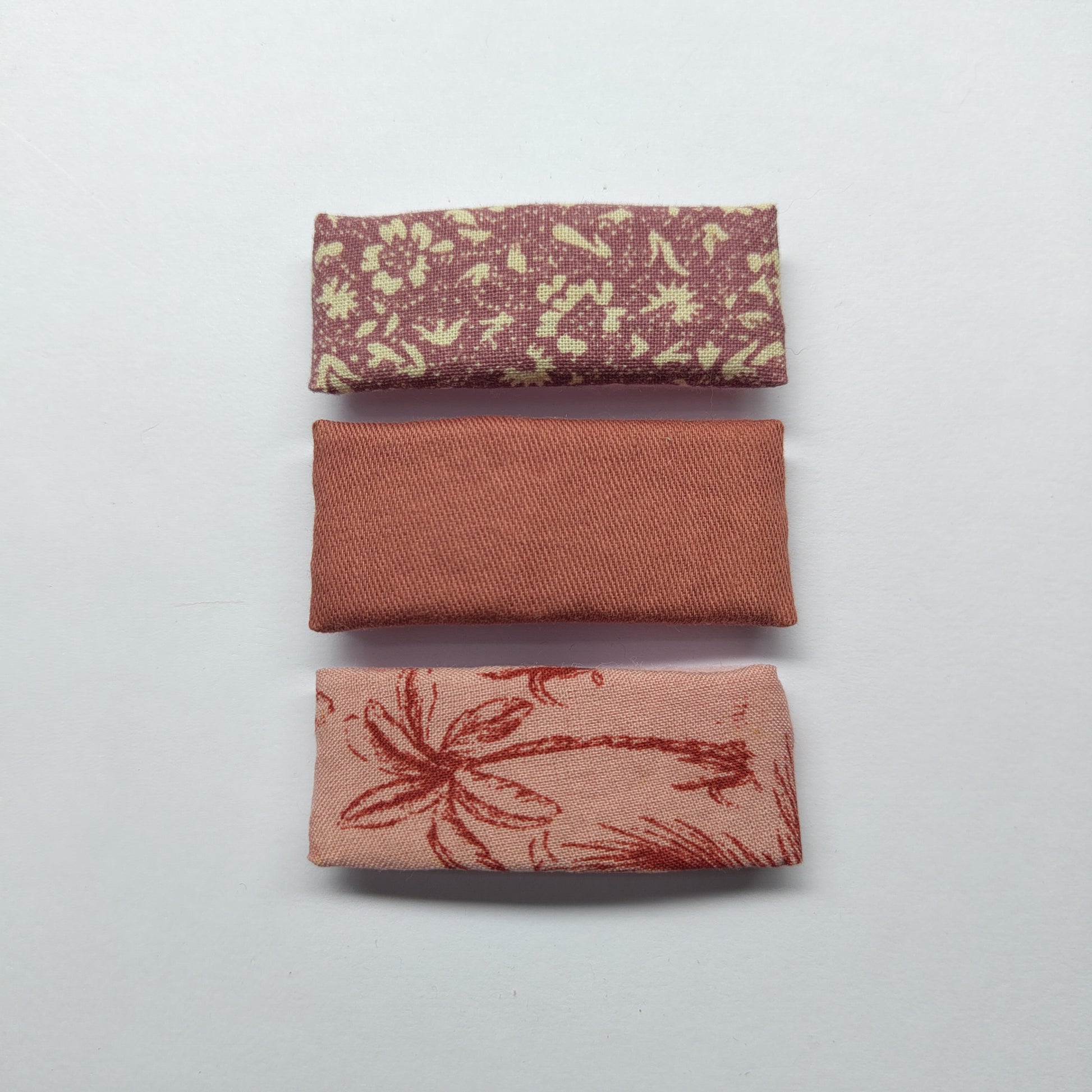 A trio of rectangular pink hair clips; floral, plain and palm tree, on a plain white background.