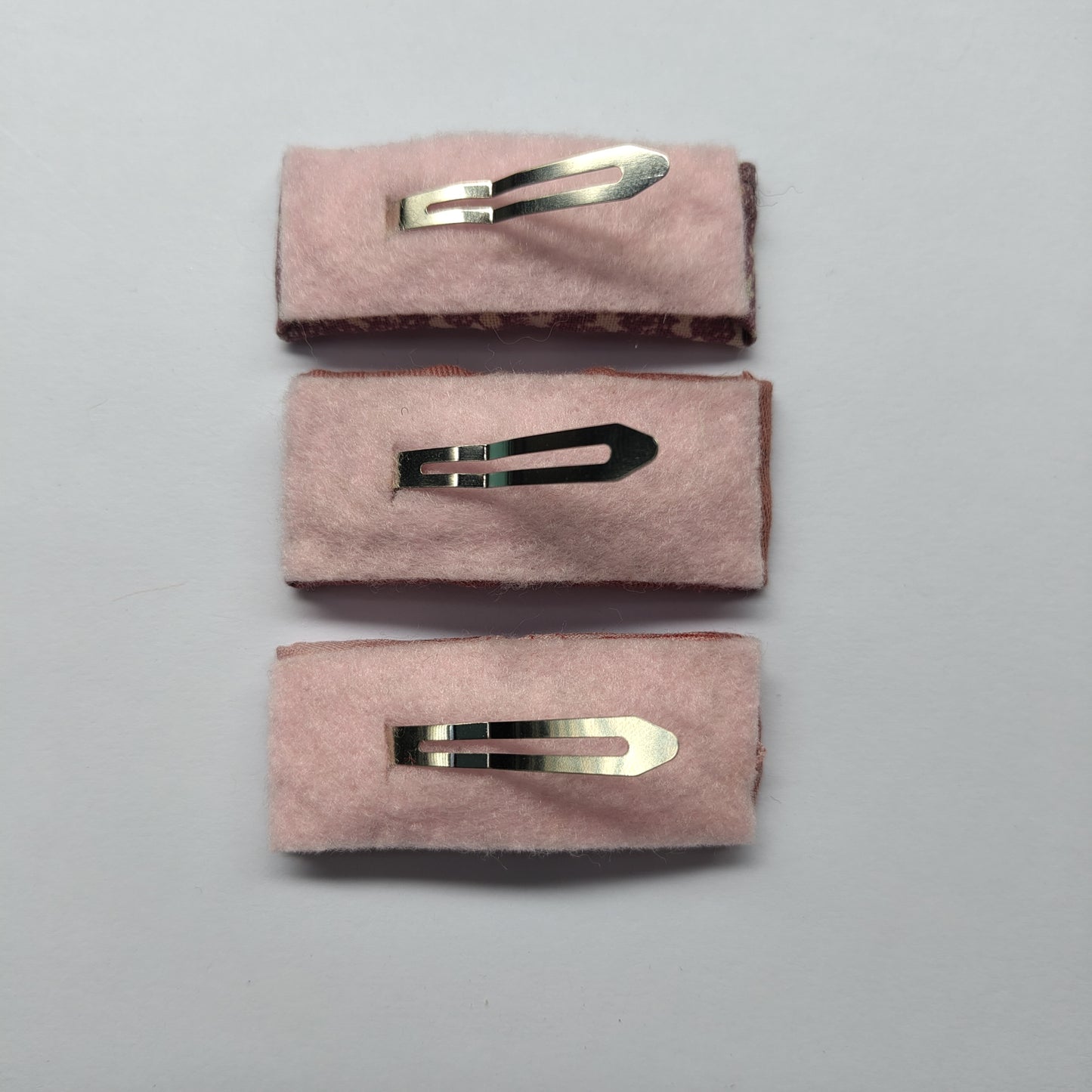 Three rectangular hair clips upside down displaying pink felt underneath and a silver prong.