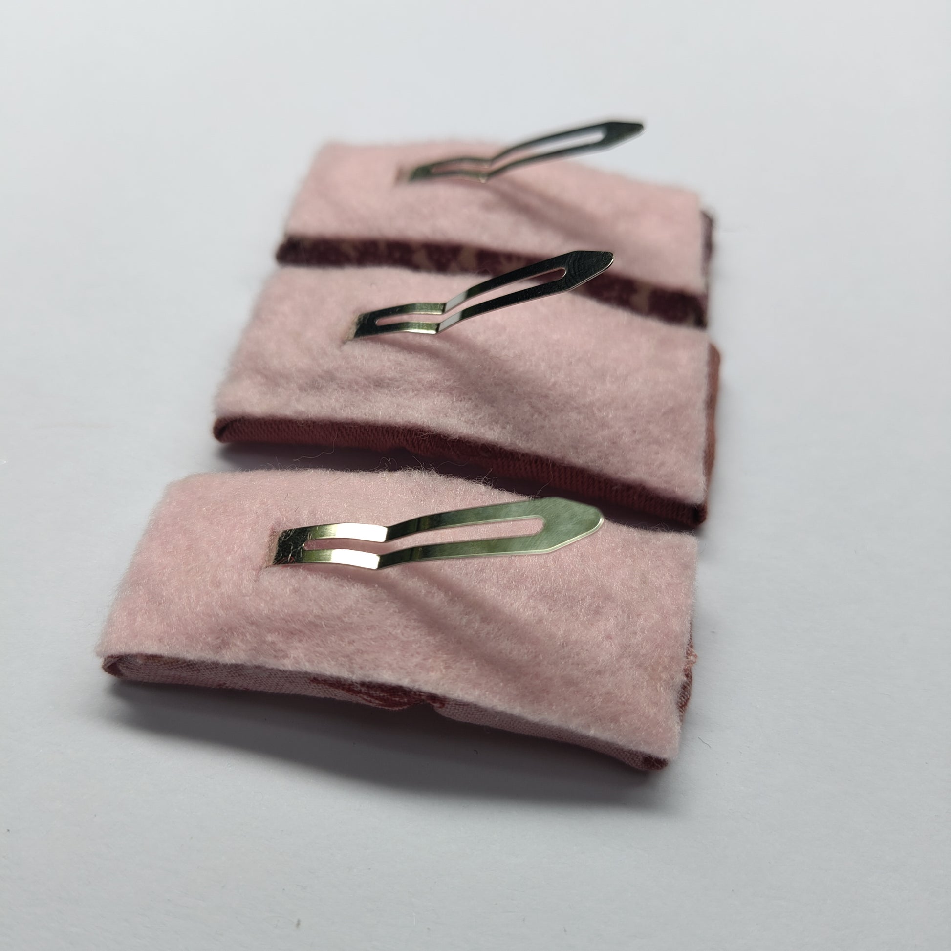 Three rectangular hair clips upside down displaying pink felt underneath and a silver prong.