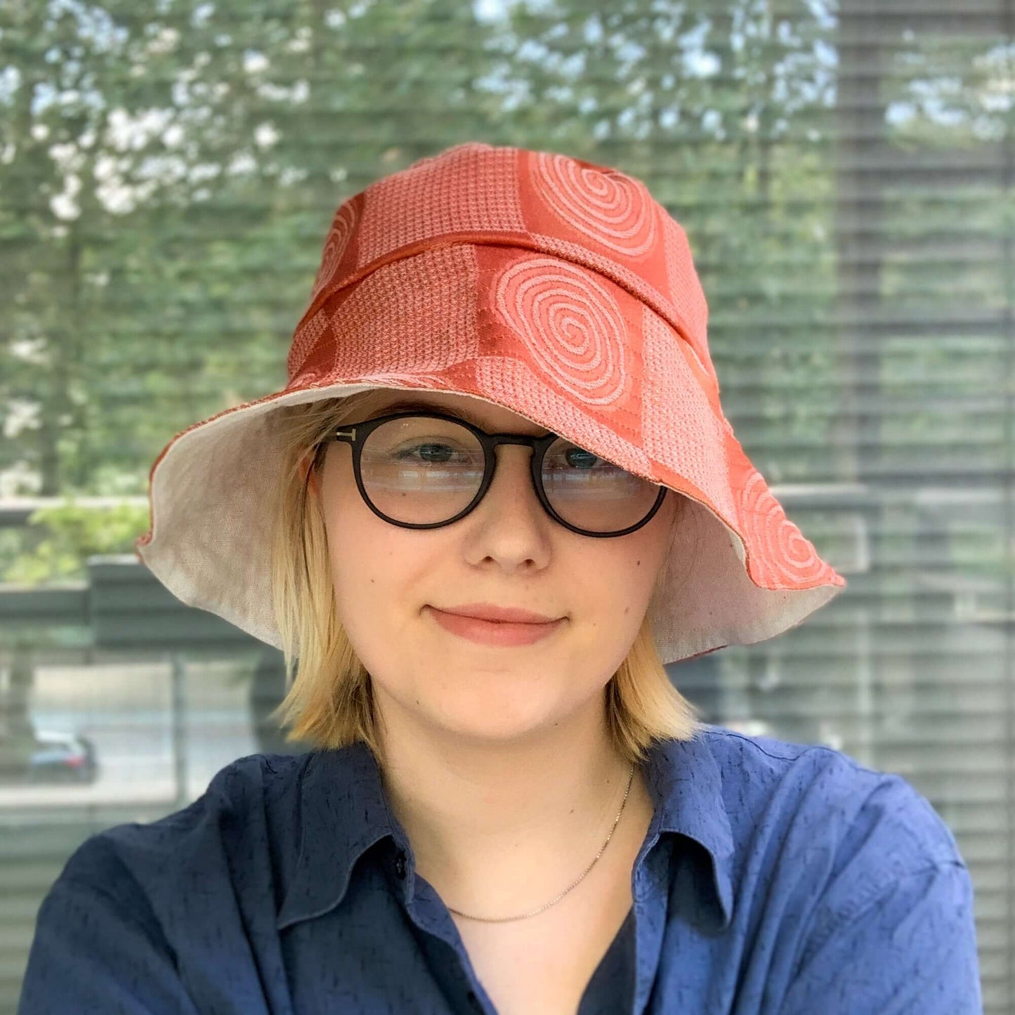 A woman in a dark blue shirt and glasses models a rust orange swirly patterned bucket sun hat while smiling