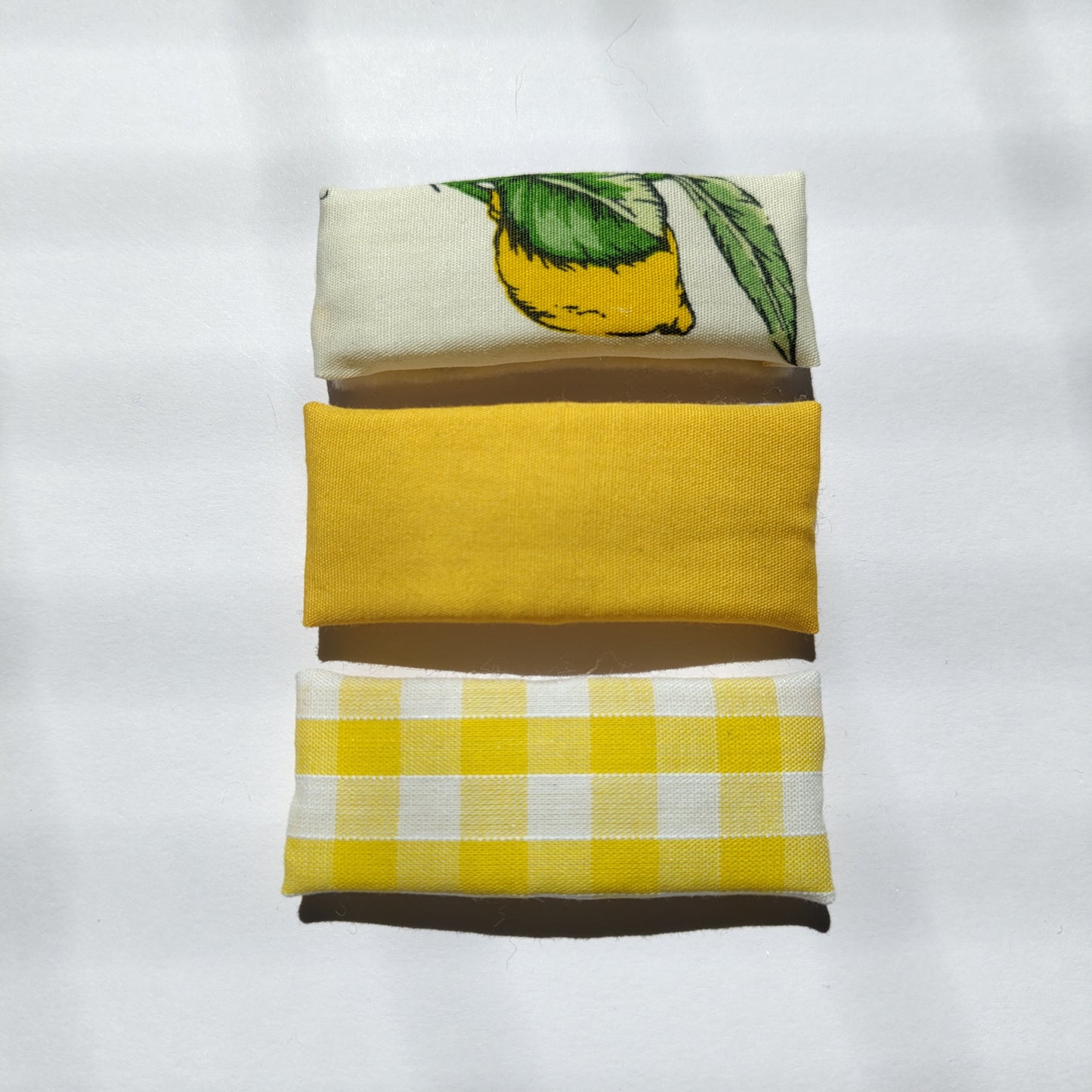 A trio of rectangular yellow hair clips; lemon print, plain and gingham, on a plain white background.