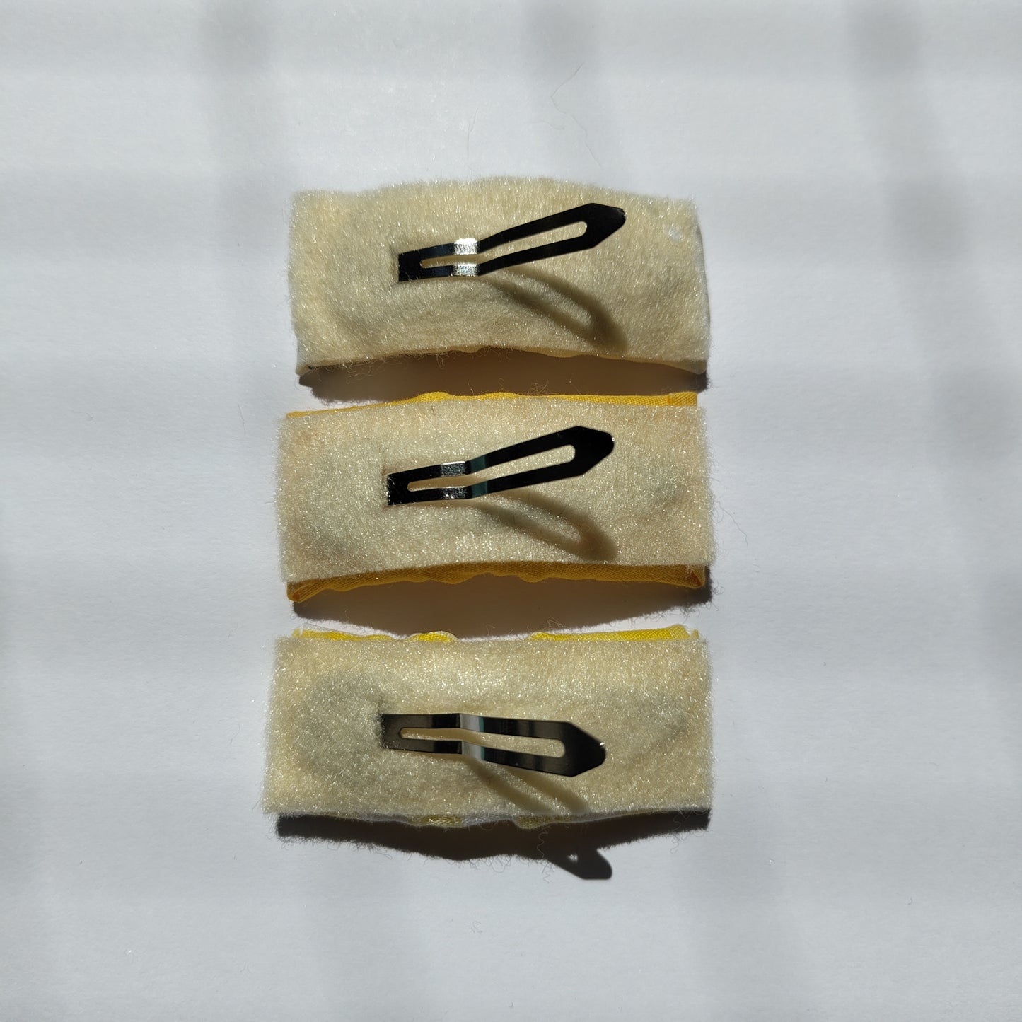 Three rectangular hair clips upside down displaying cream felt underneath and a silver prong.