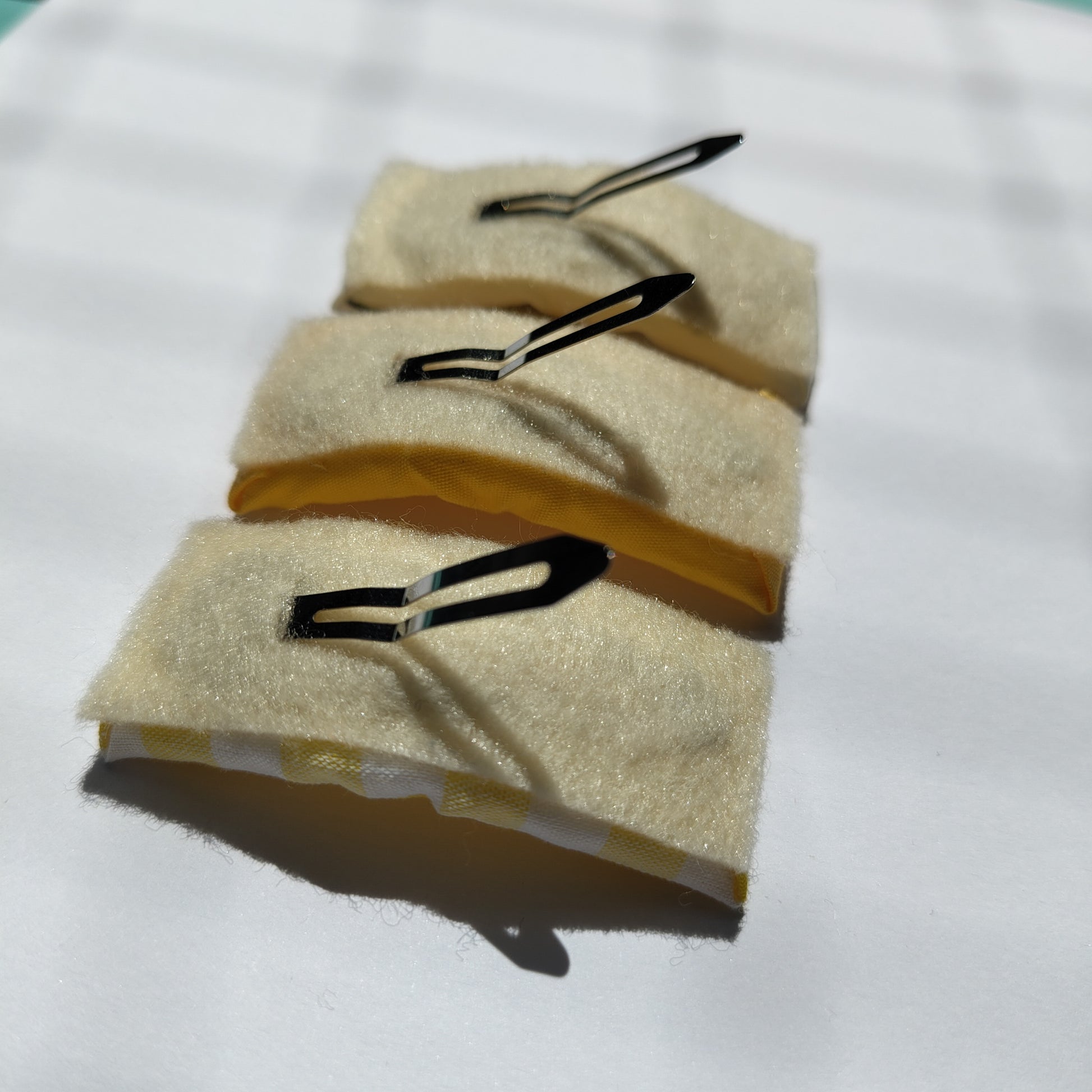 Three rectangular hair clips upside down displaying cream felt underneath and a silver prong.