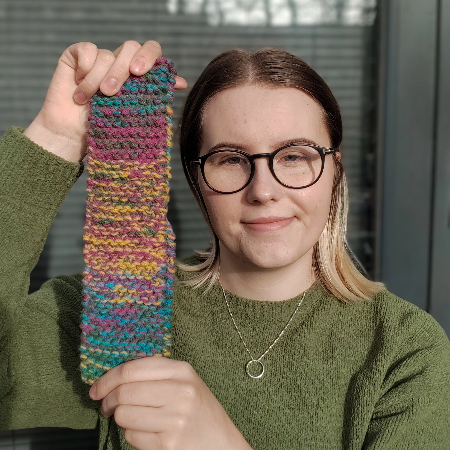 A woman holds up a multicolour knitted ear warmer headband