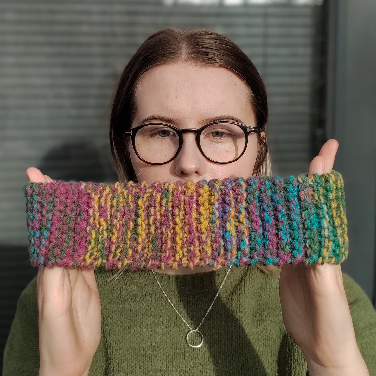 A woman models a multicolour knitted ear warmer headband between her hands