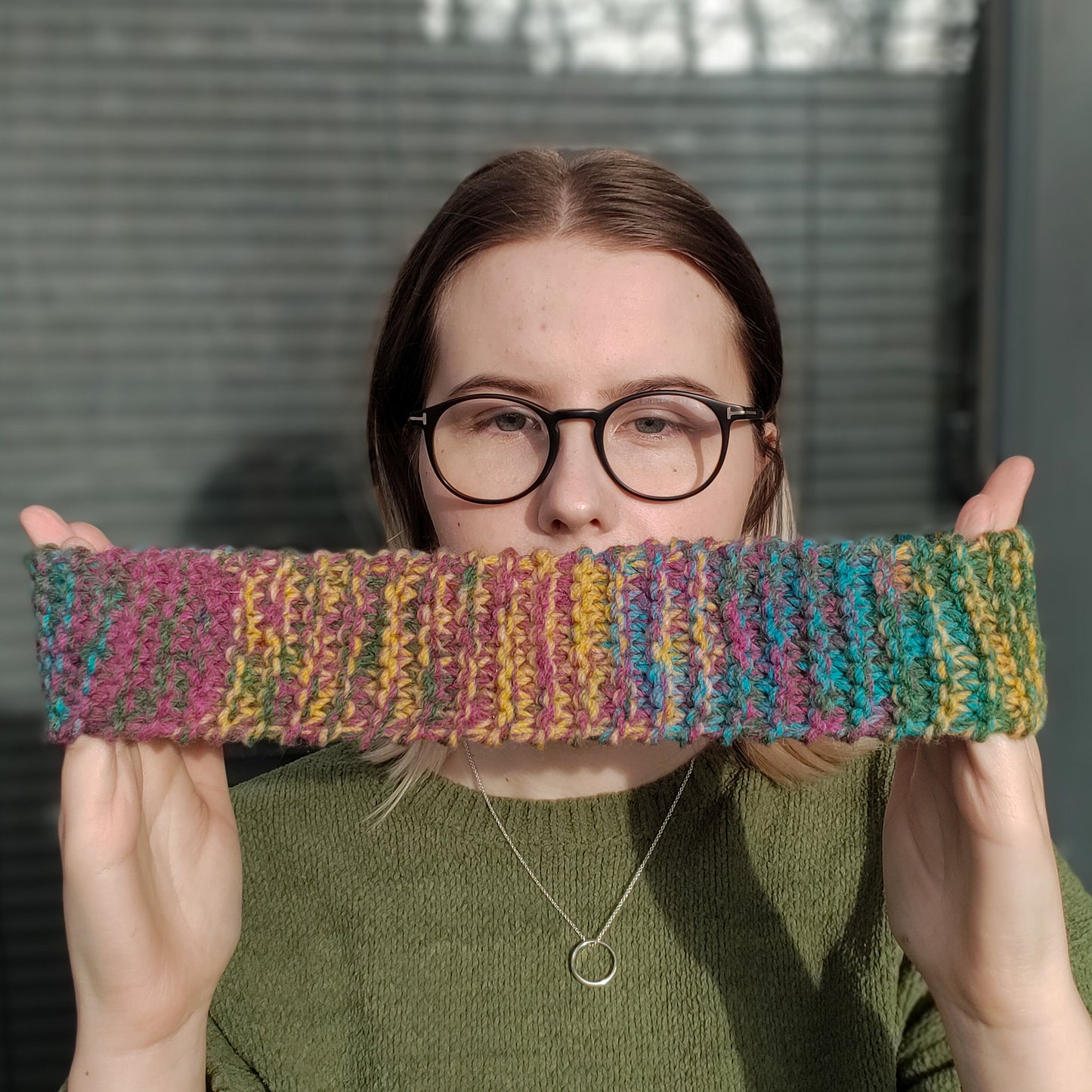 A woman models a multicolour knitted ear warmer headband stretched between her hands