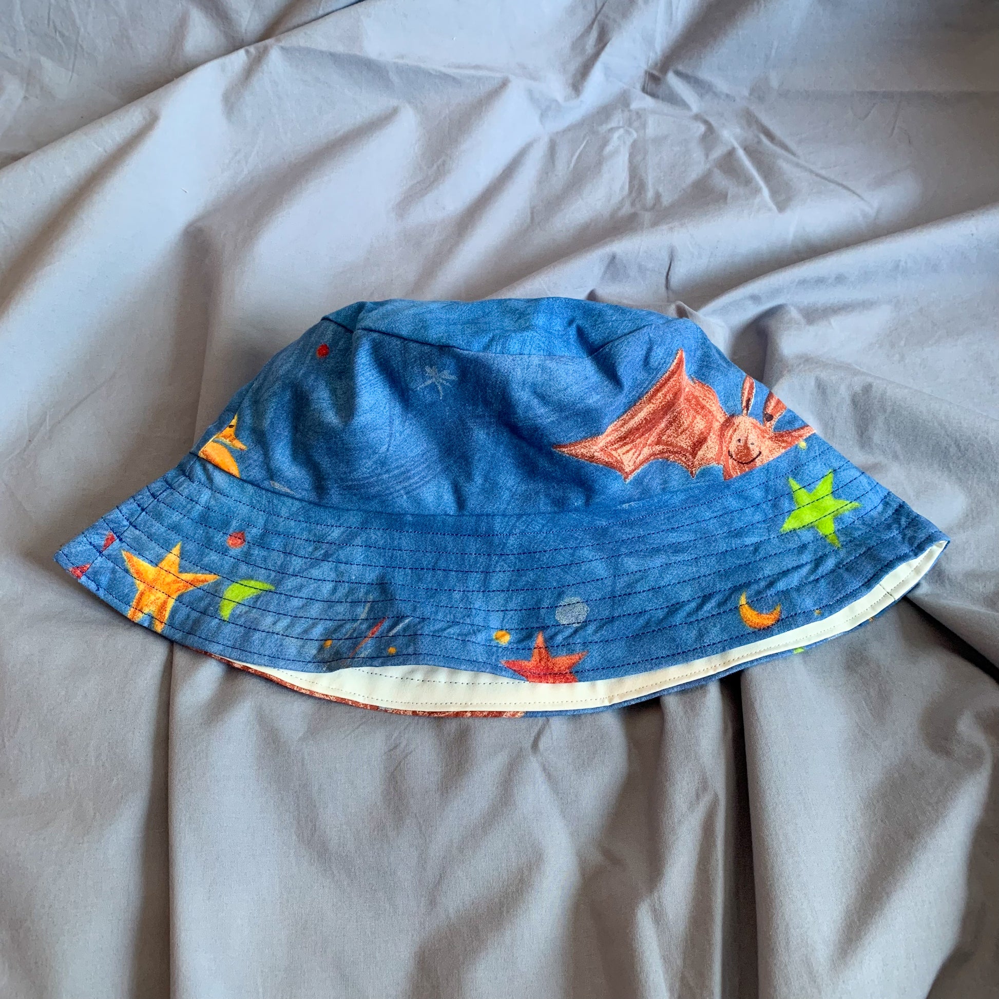 A blue bucket hat with part of a cartoon bat folded in half sat on a blue background