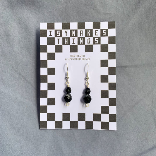 Black gem earrings on a checkerboard backing against a blue background