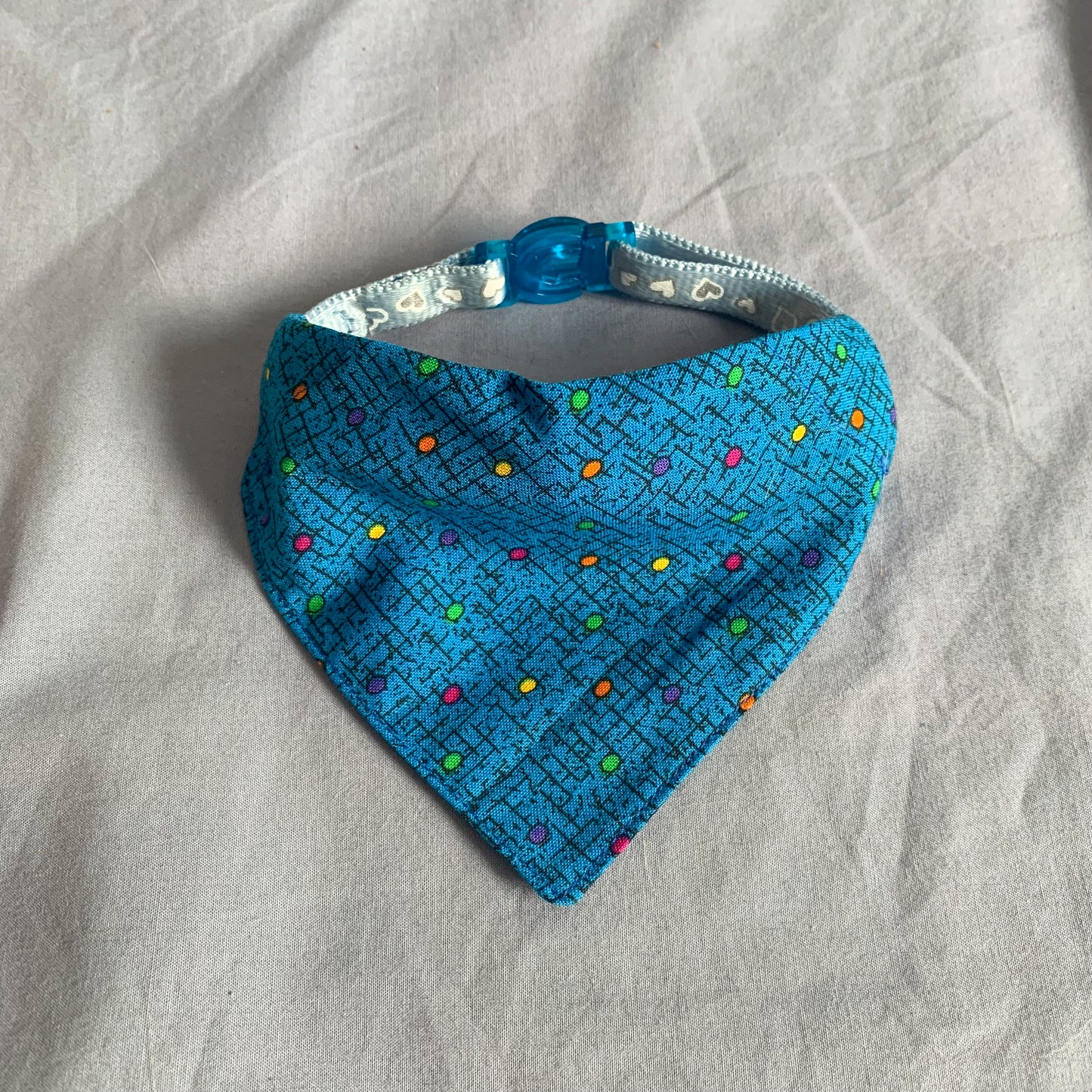 a blue dotted triangle cat bandana on a blue collar sat on a blue background