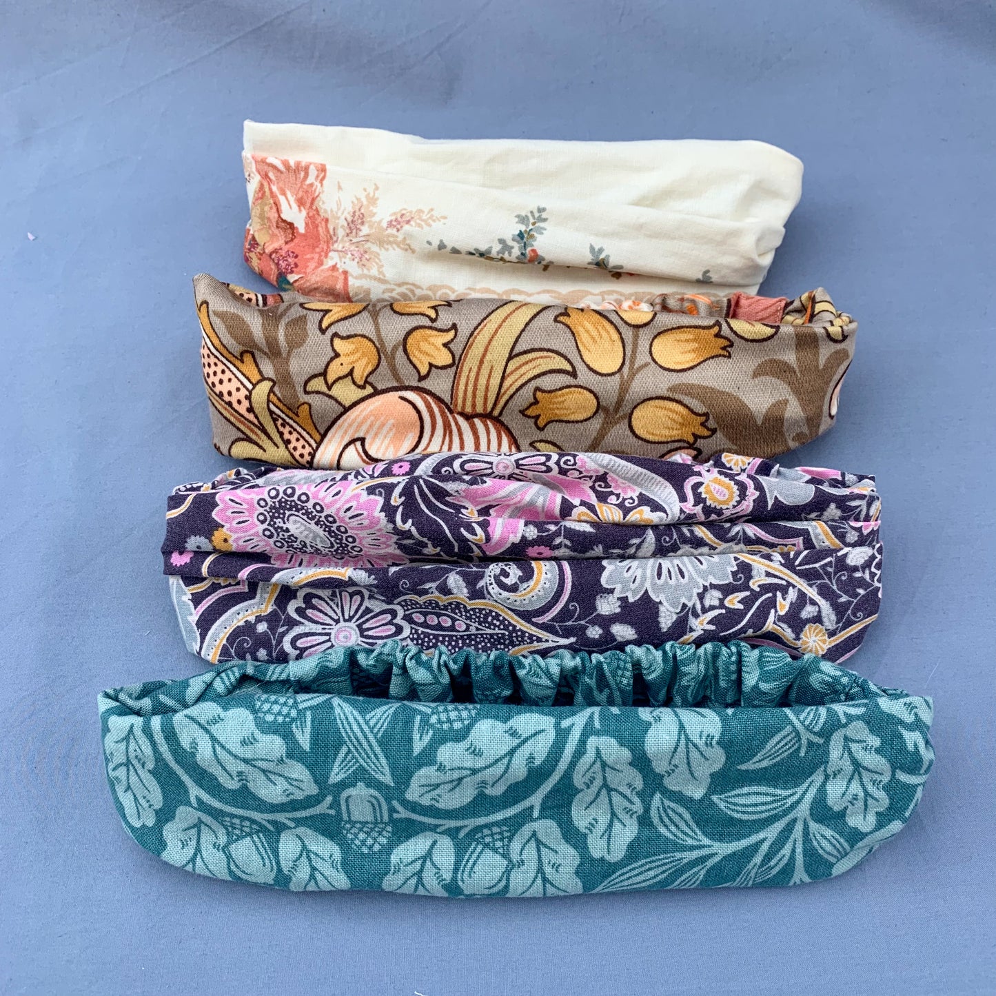 four folded bandanas, from top to bottom cream, brown, purple and blue, all against a blue background