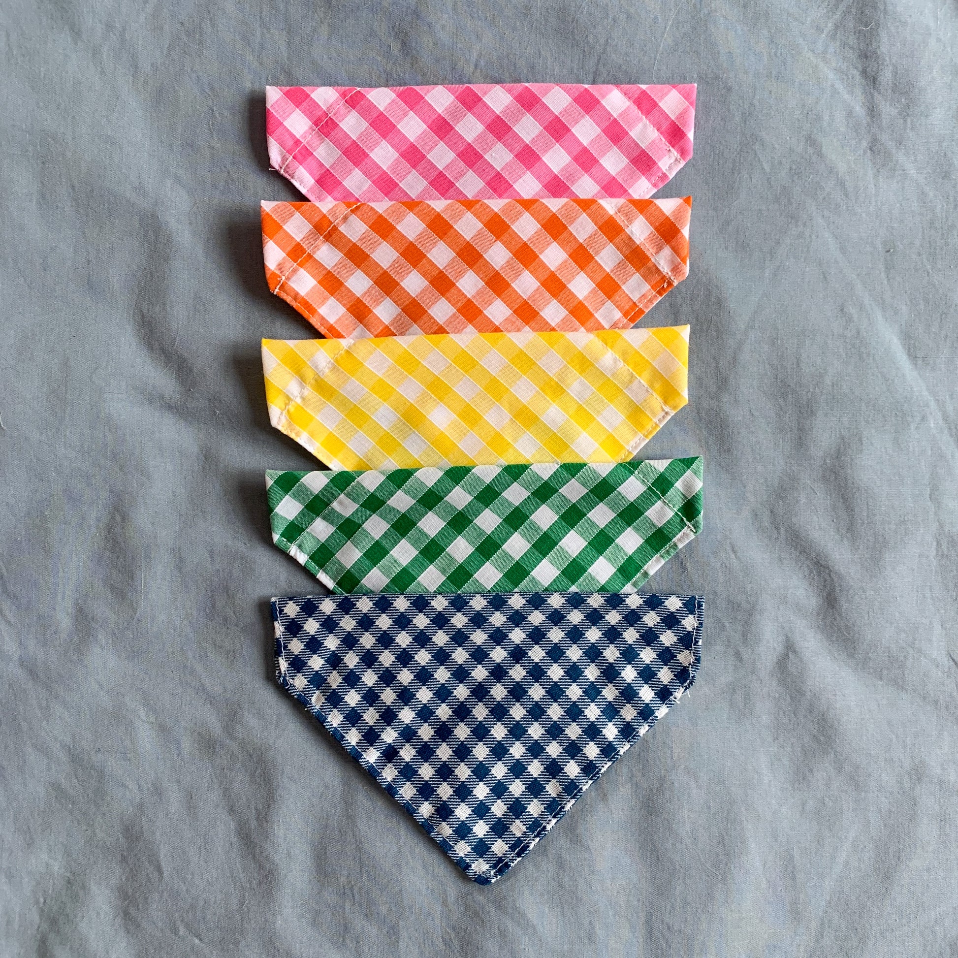 triangle gingham pet bandanas in a line, pink, orange, yellow, green and blue 