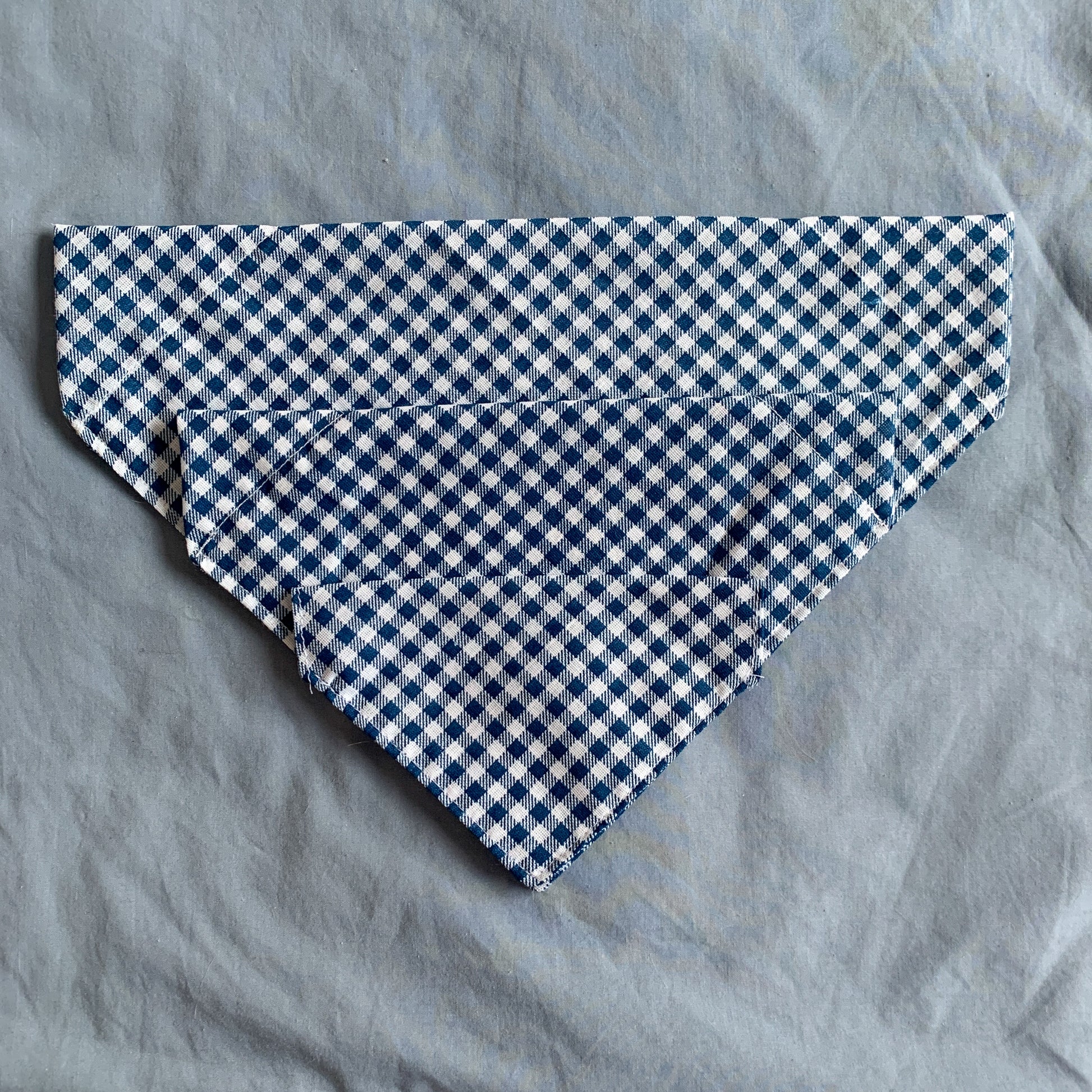 three different sized blue gingham triangle pet bandanas sit atop each other