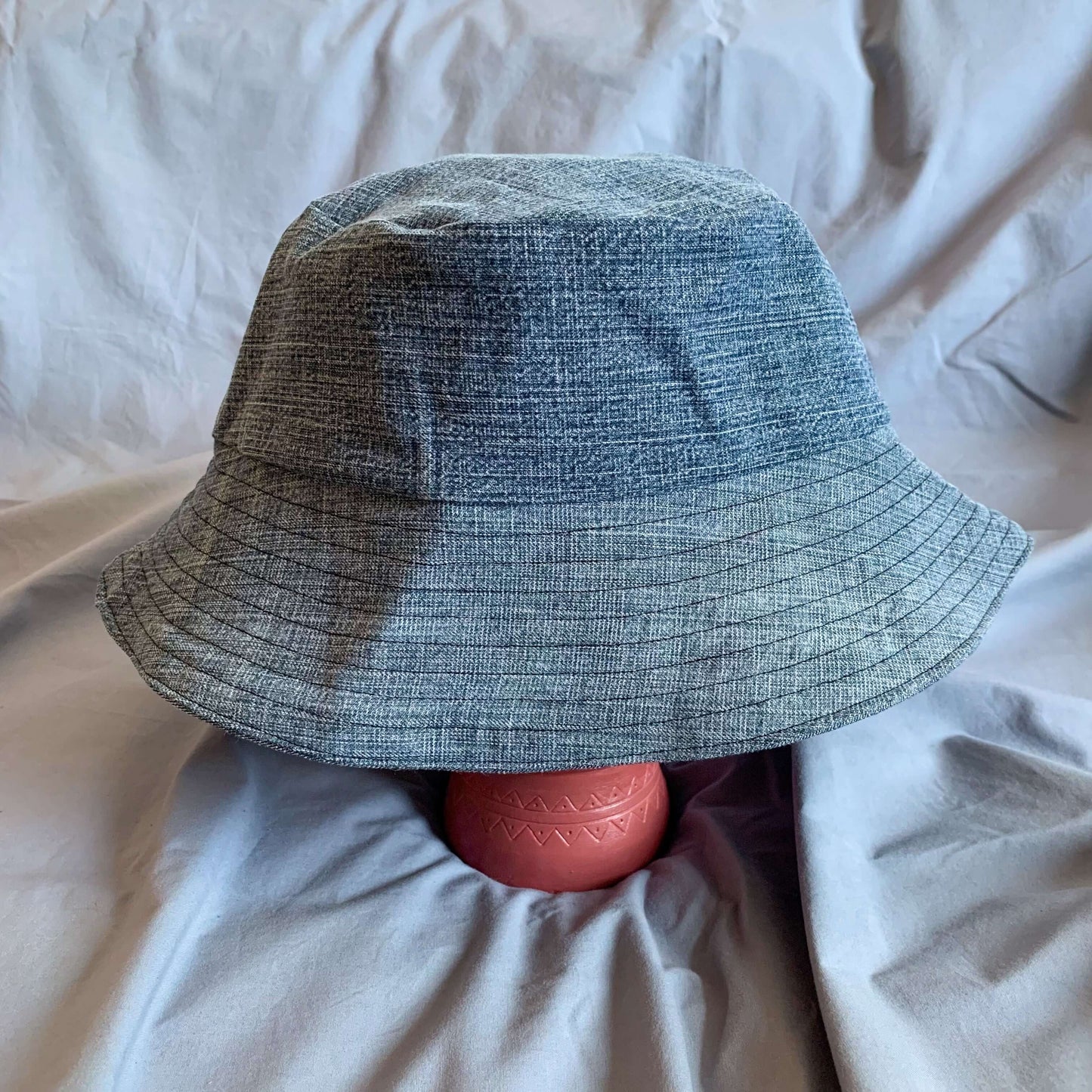 Blue denim bucket hat styled on a pink painted stone face against a blue background