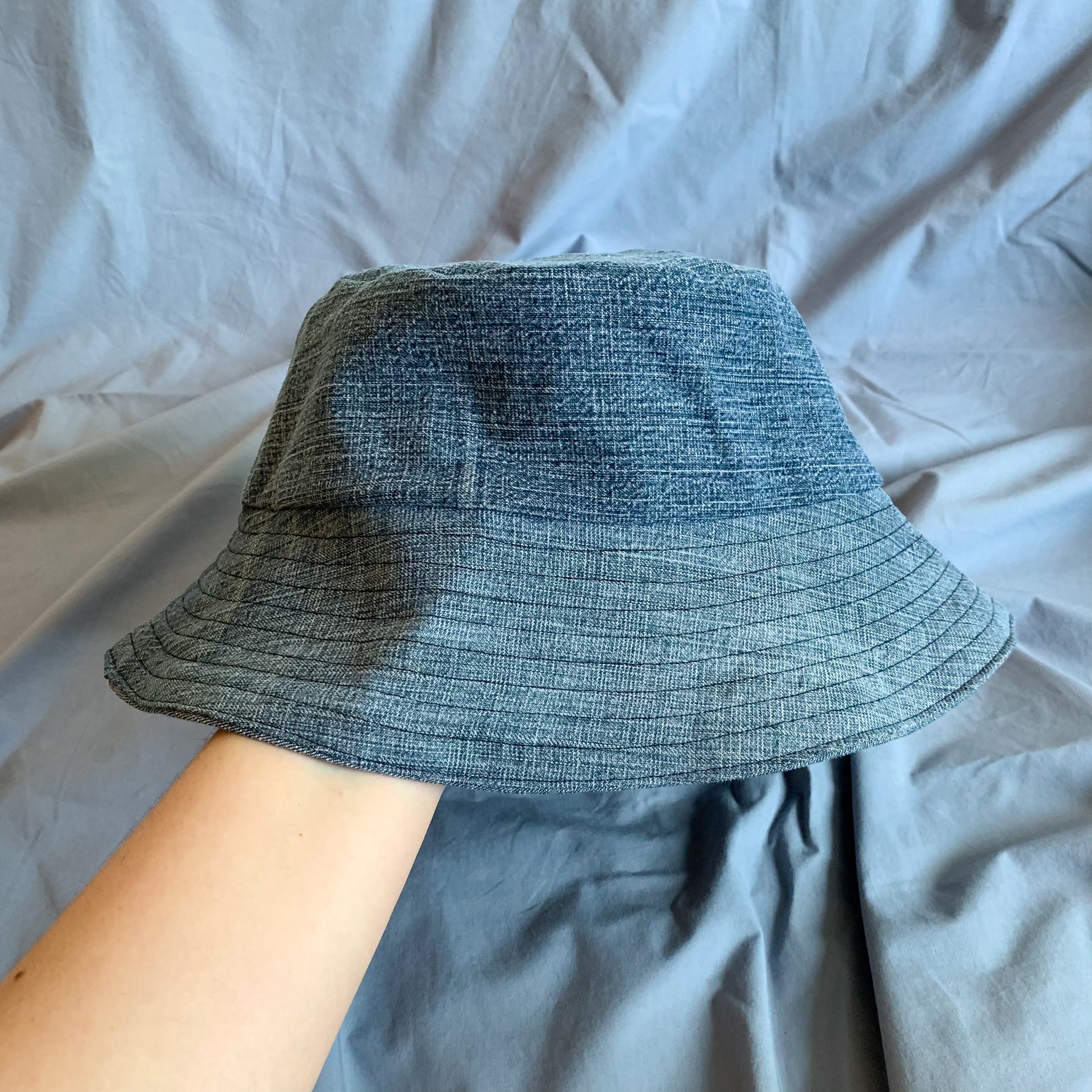 A blue denim bucket hat held in a white persons arm against a blue background