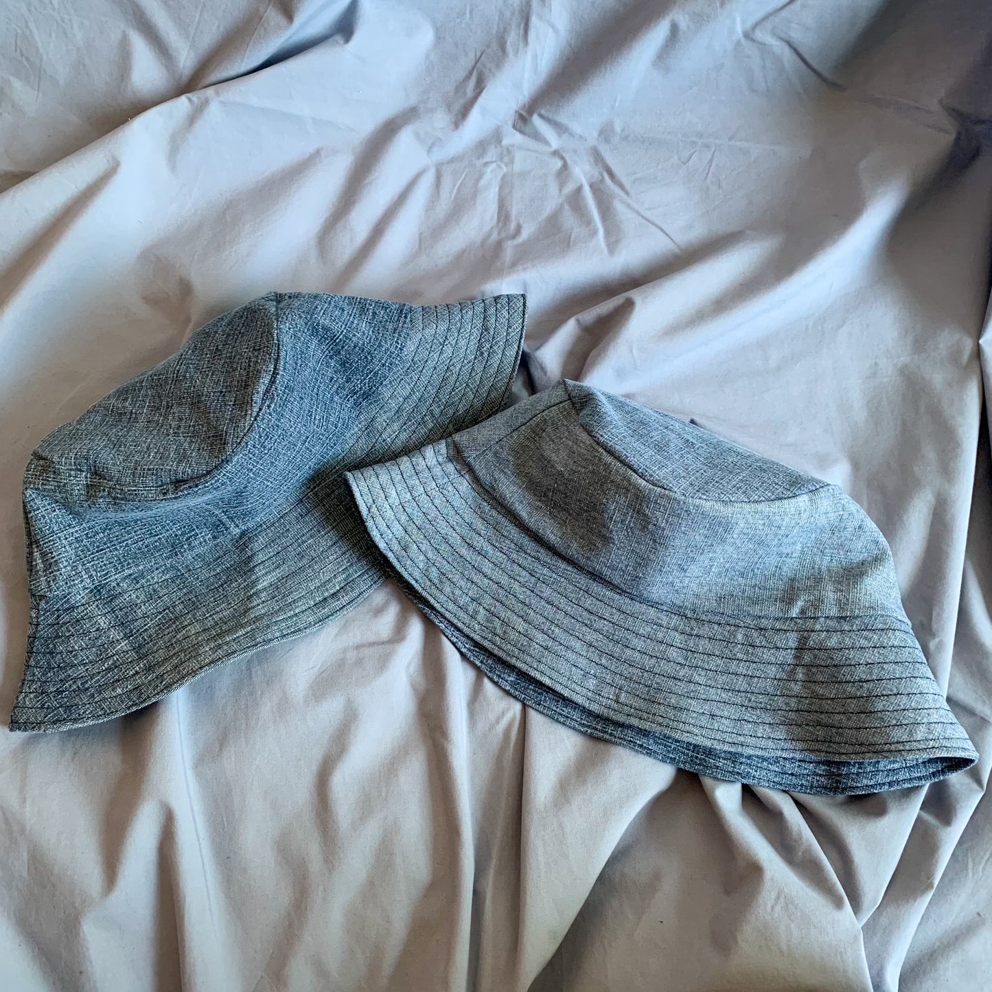 Two folded denim bucket hats laying down on a blue background