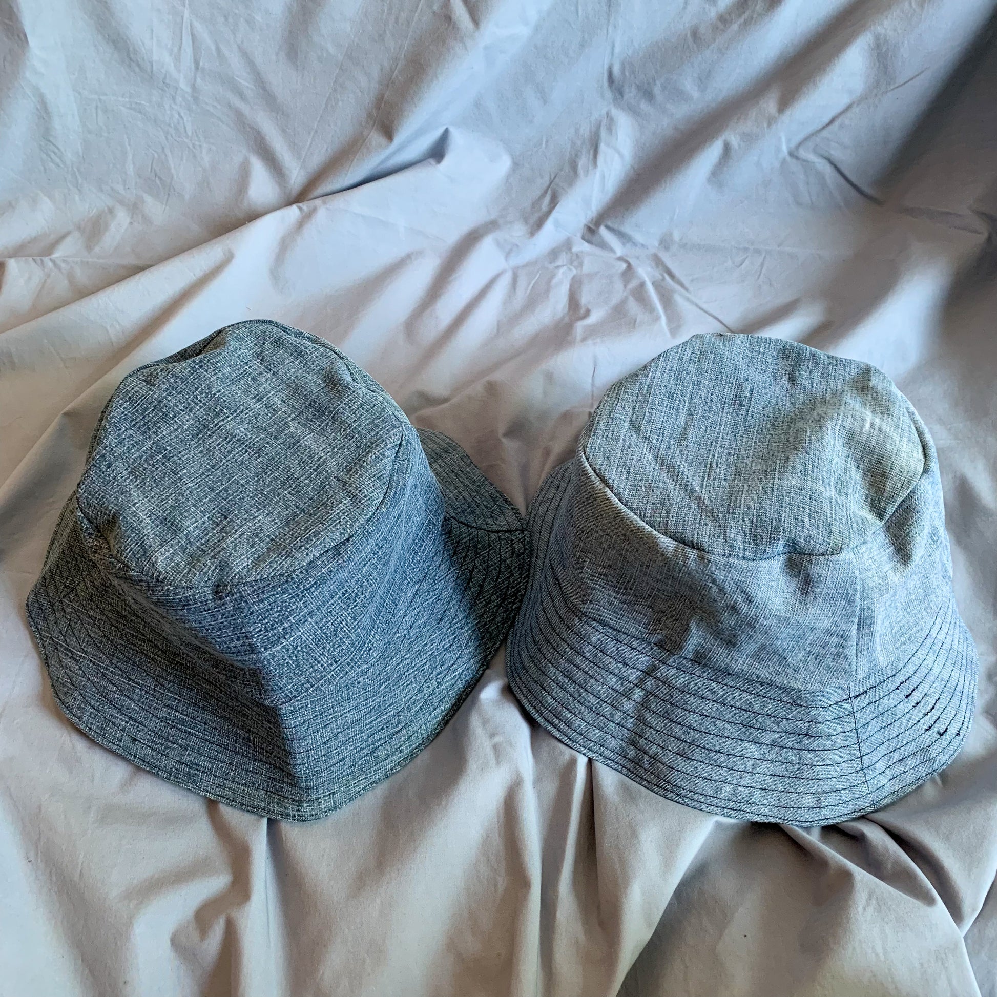 Two denim bucket hats, the left one darker and right one lighter sat upright against a blue background