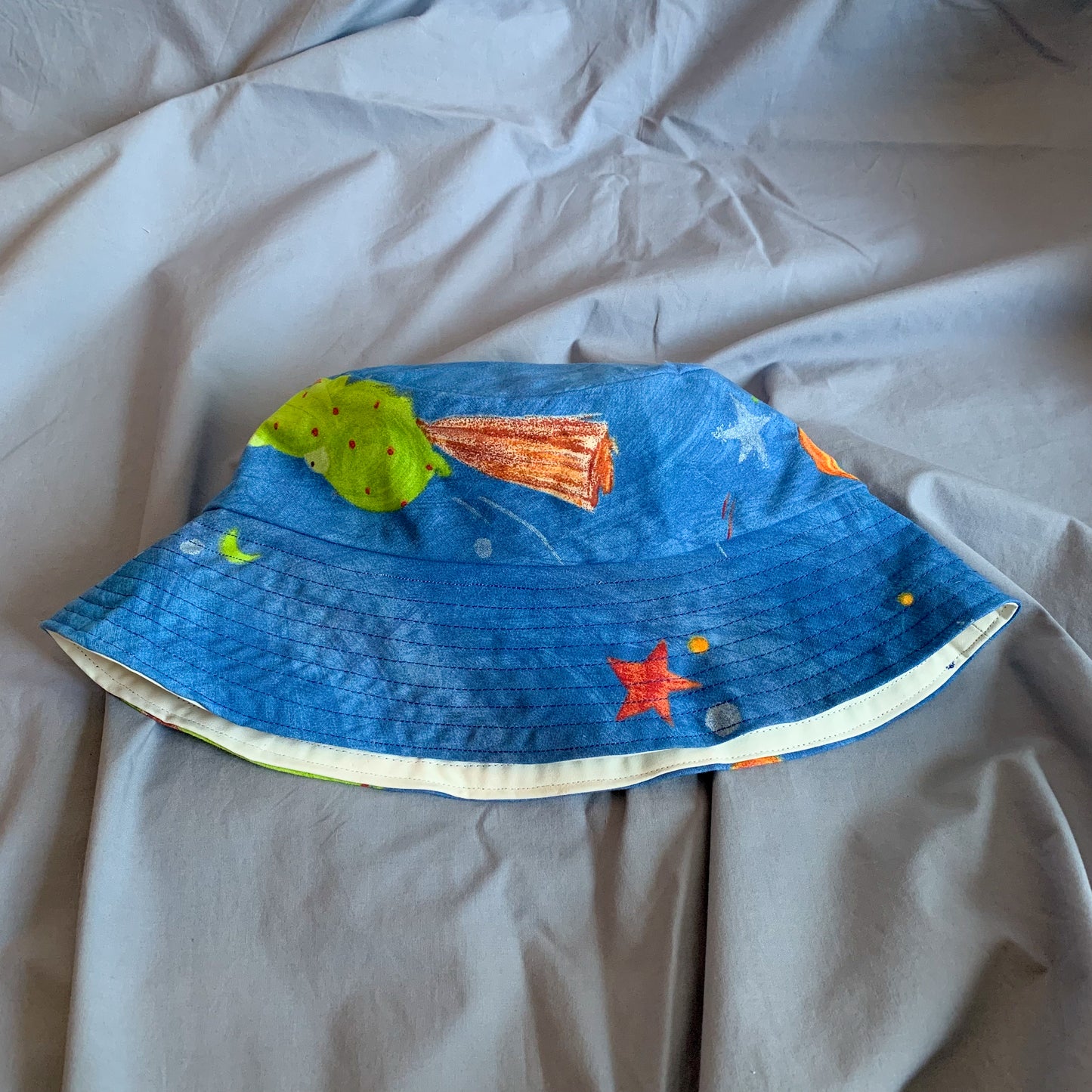 A blue bucket hat with part of a cartoon frog folded in half sat on a blue background