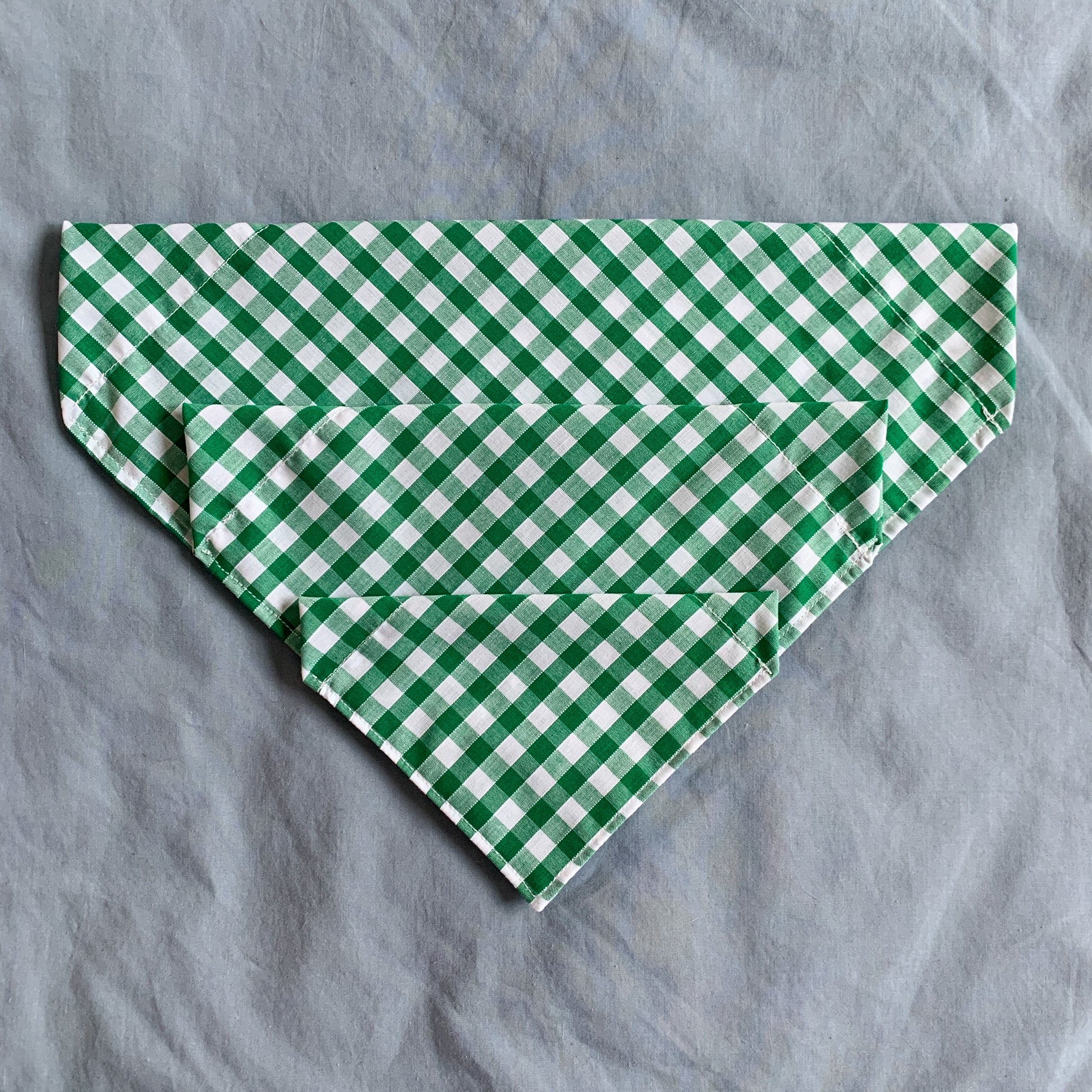 three different sized green gingham triangle pet bandanas sit atop each other