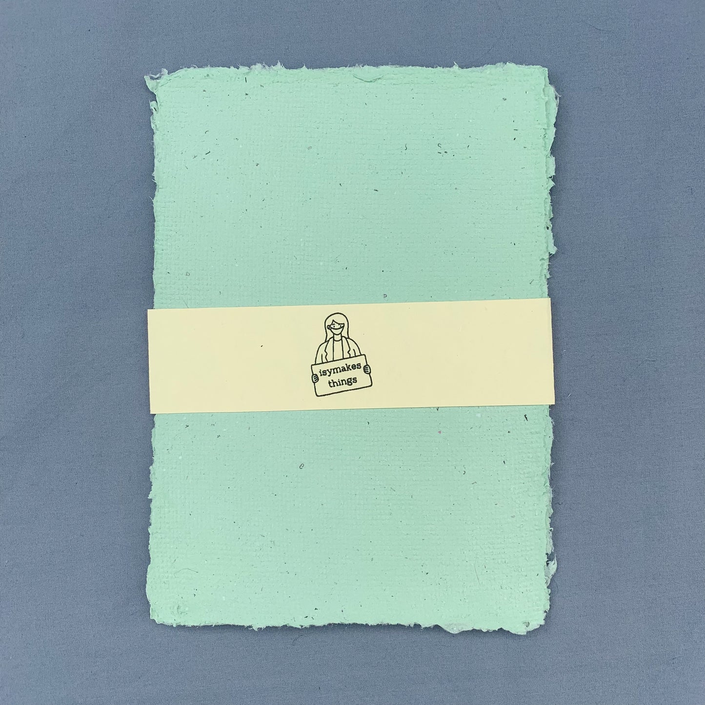 a stack of green sheets of paper with a cream coloured isymakesthings logo sleeve around them against a blue background