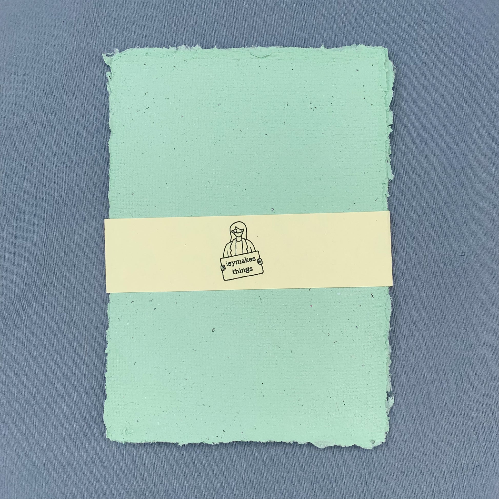 a stack of green sheets of paper with a cream coloured isymakesthings logo sleeve around them against a blue background