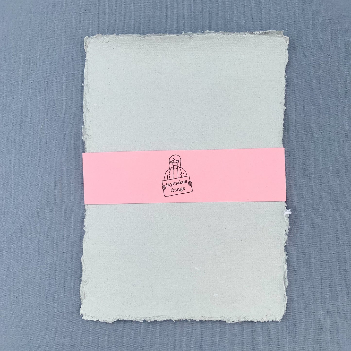 a stack of grey sheets of paper with a pink coloured isymakesthings logo sleeve around them against a blue background