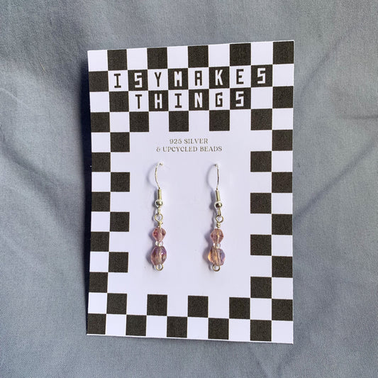 Purple gem earrings on a checkerboard backing against a blue background