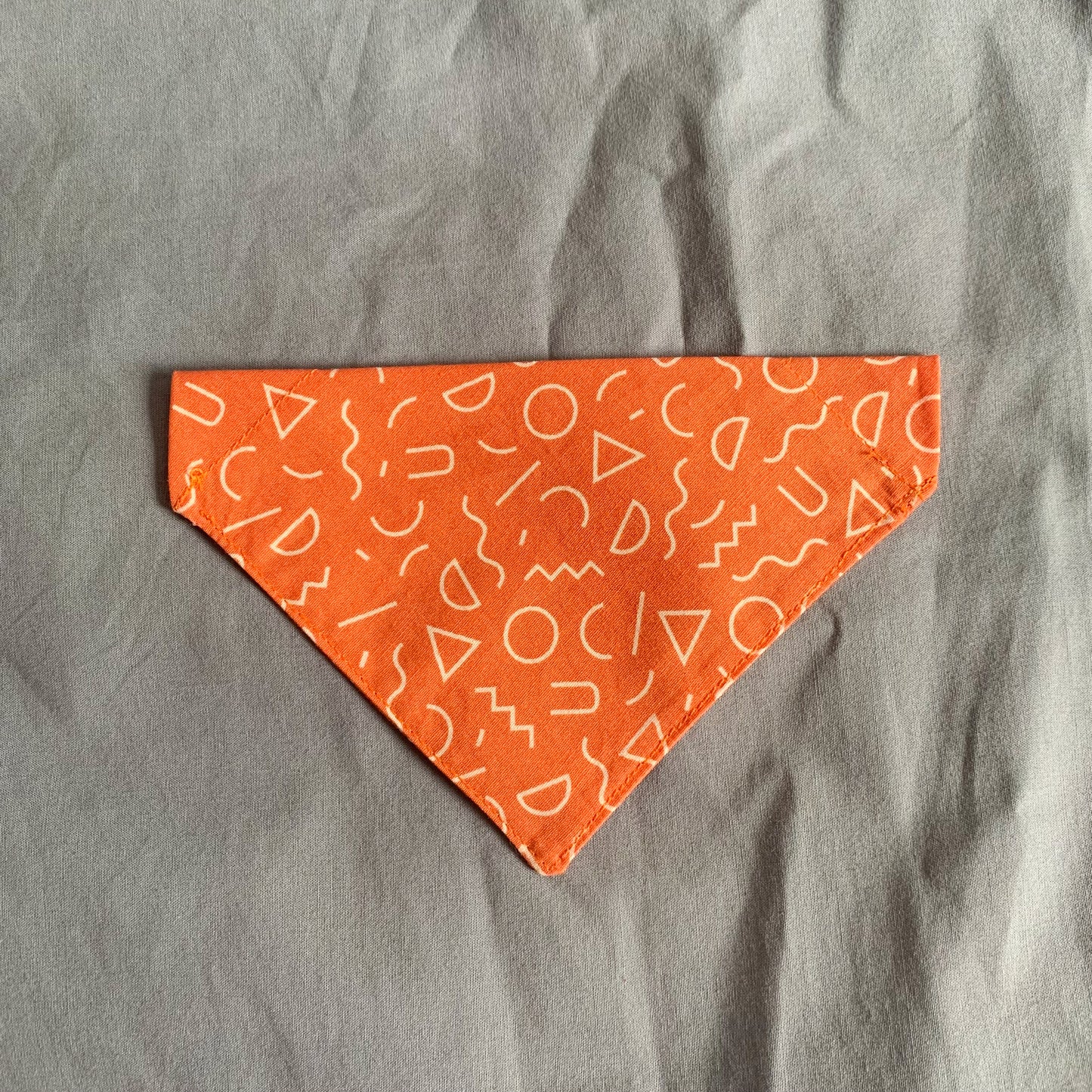 An orange triangle cat bandana laying on a blue background