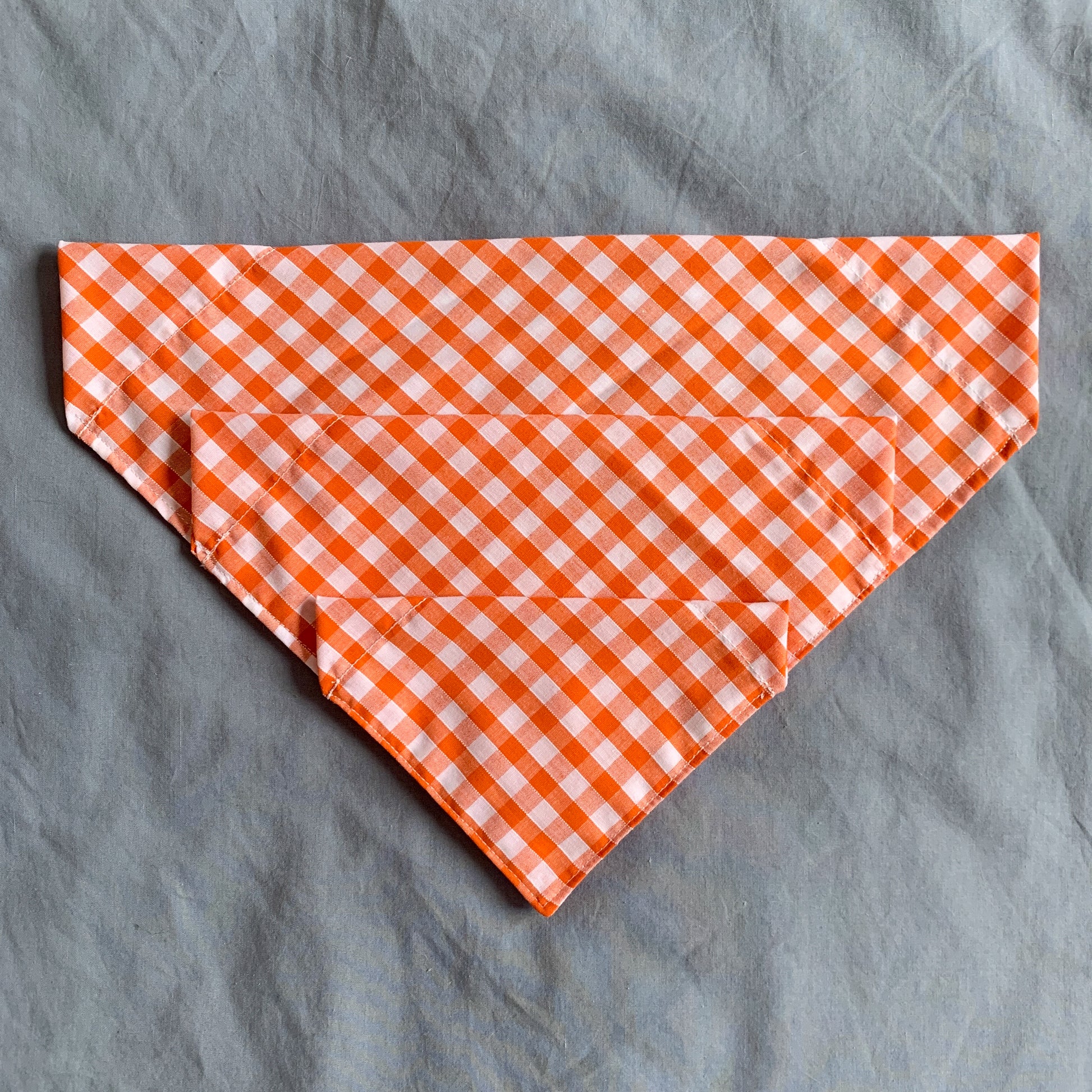 three different sized orange gingham triangle pet bandanas sit atop each other