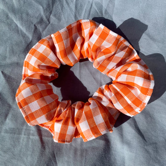 A single orange gingham check scrunchie on a blue background