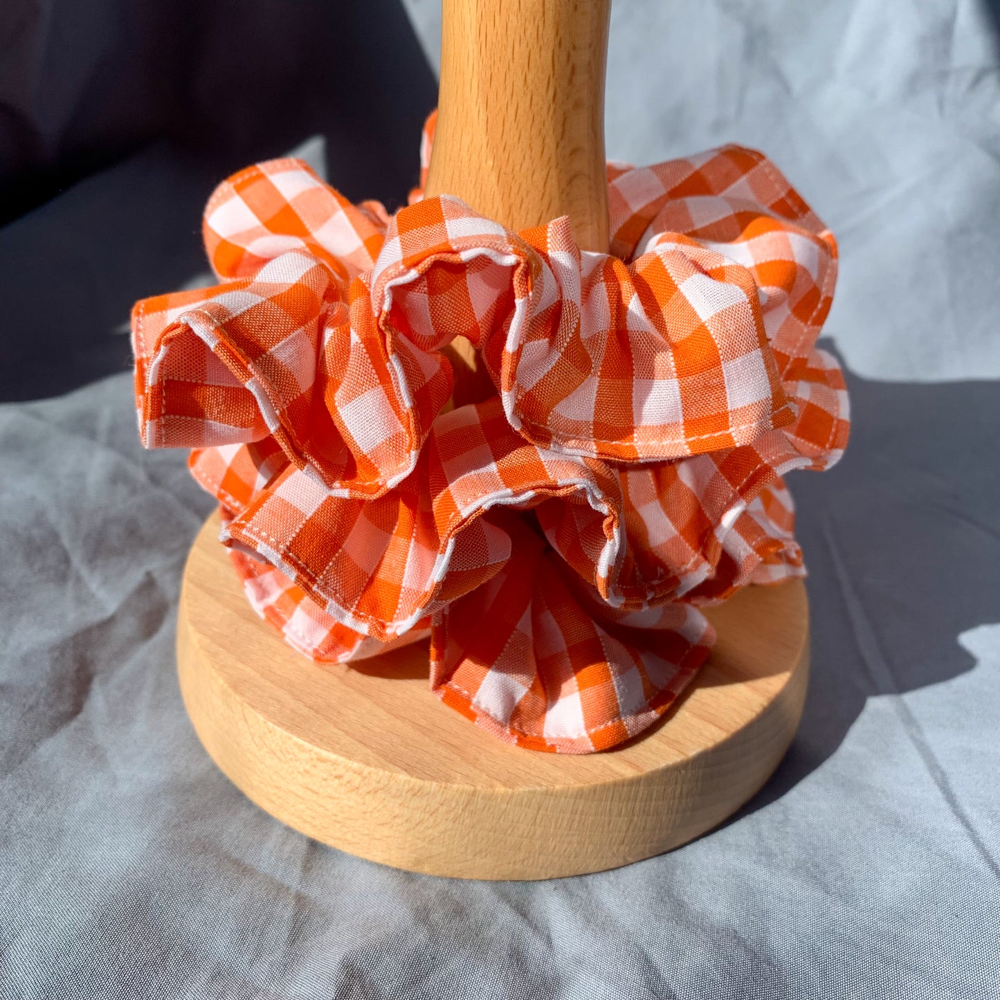 A stack of three orange gingham scrunchies on a wooden pole against a blue background