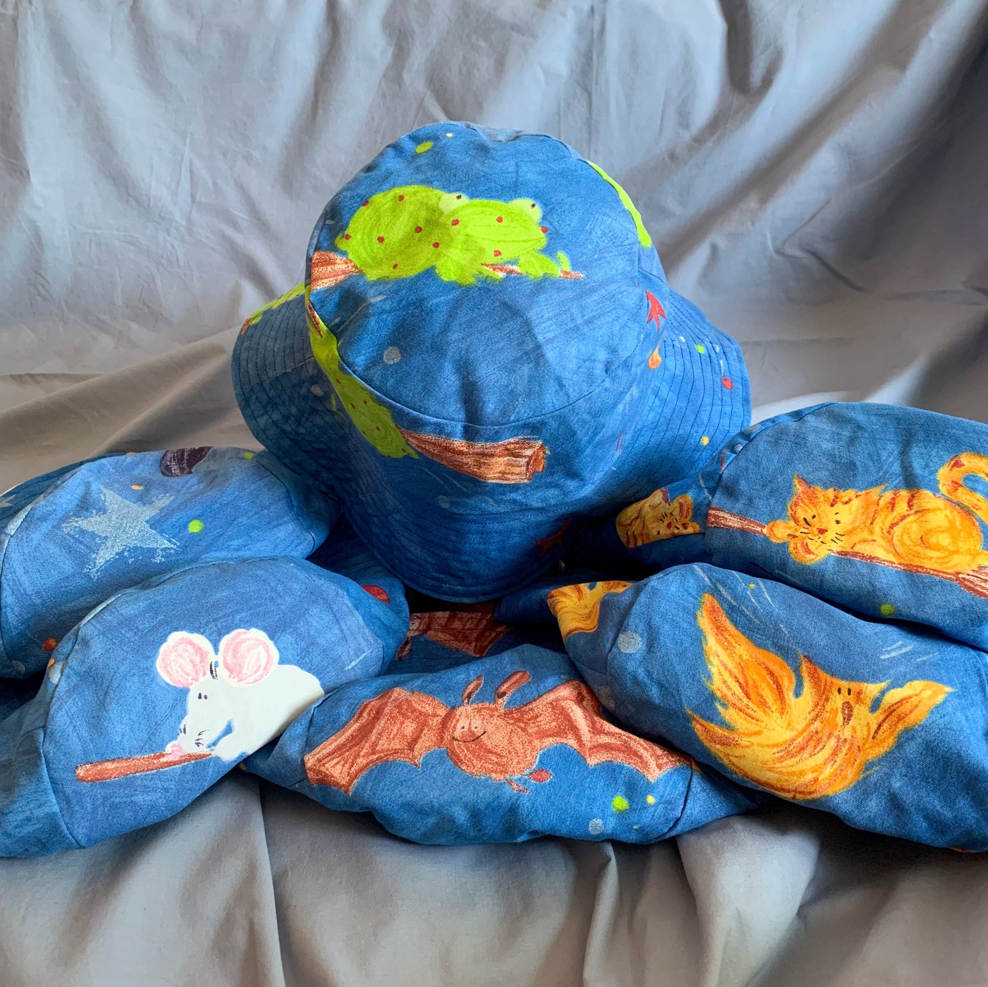 Six blue bucket hats each with a cartoon character on top: plain, mouse, frog, bat, cat, phoenix, sat on a blue background