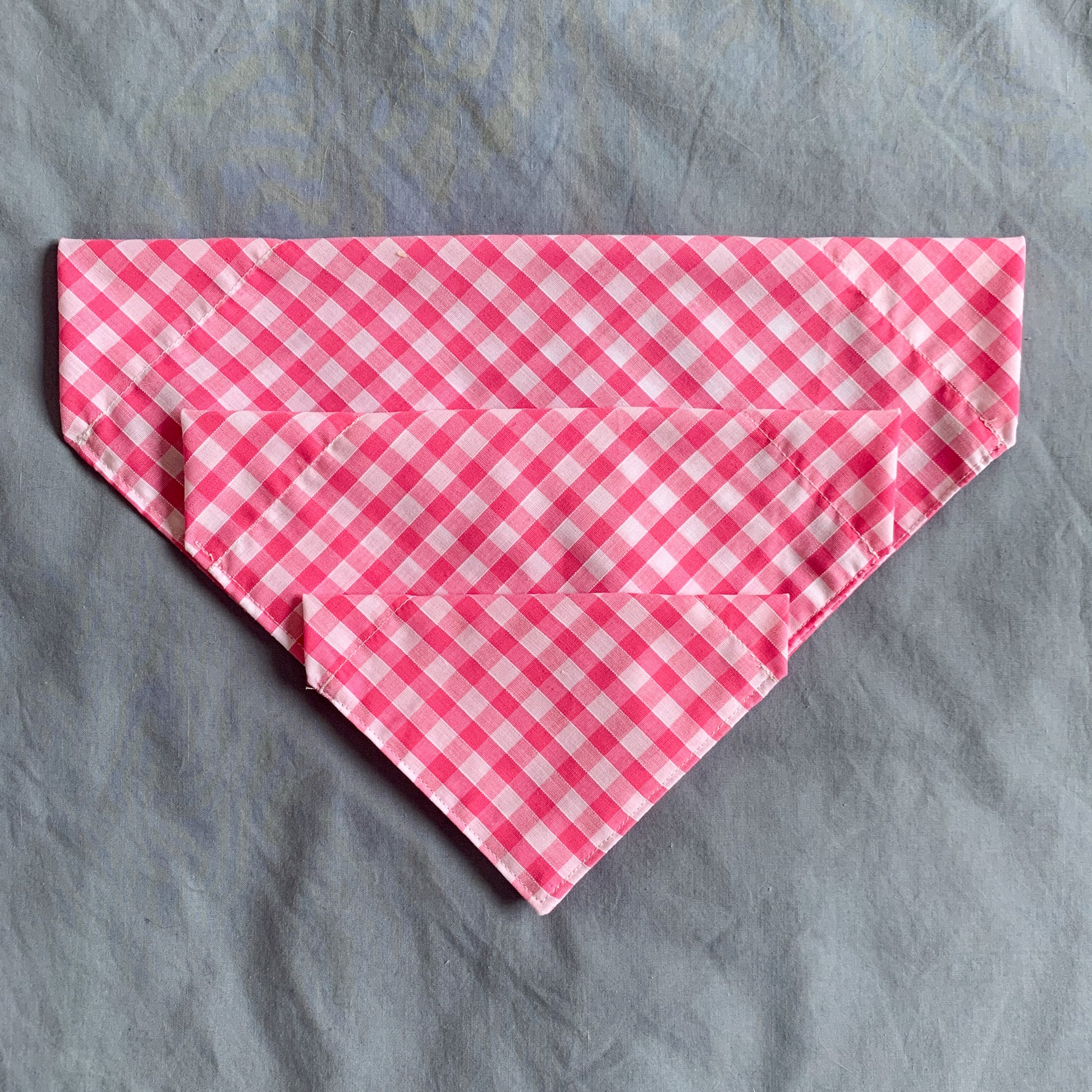 three different sized pink gingham triangle bandanas sit atop each other