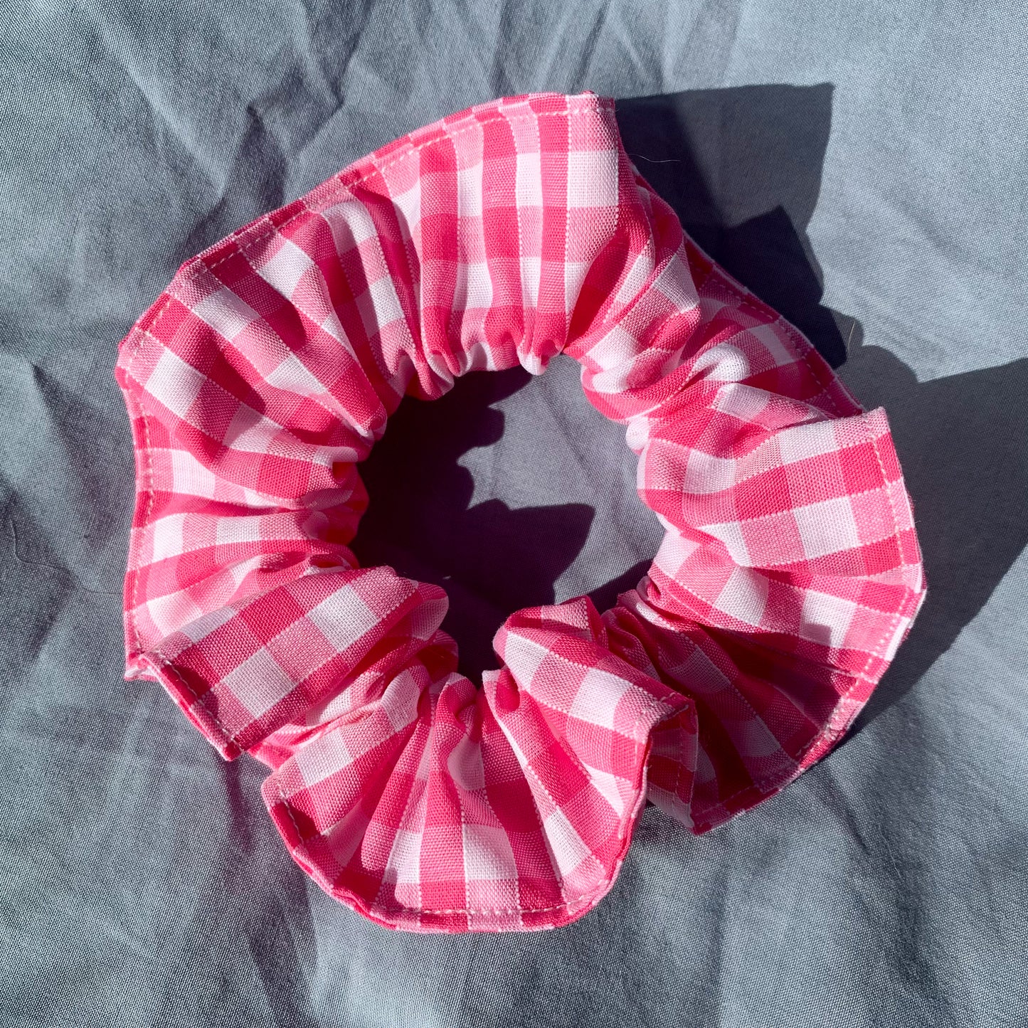 A single pink gingham check scrunchie on a blue background