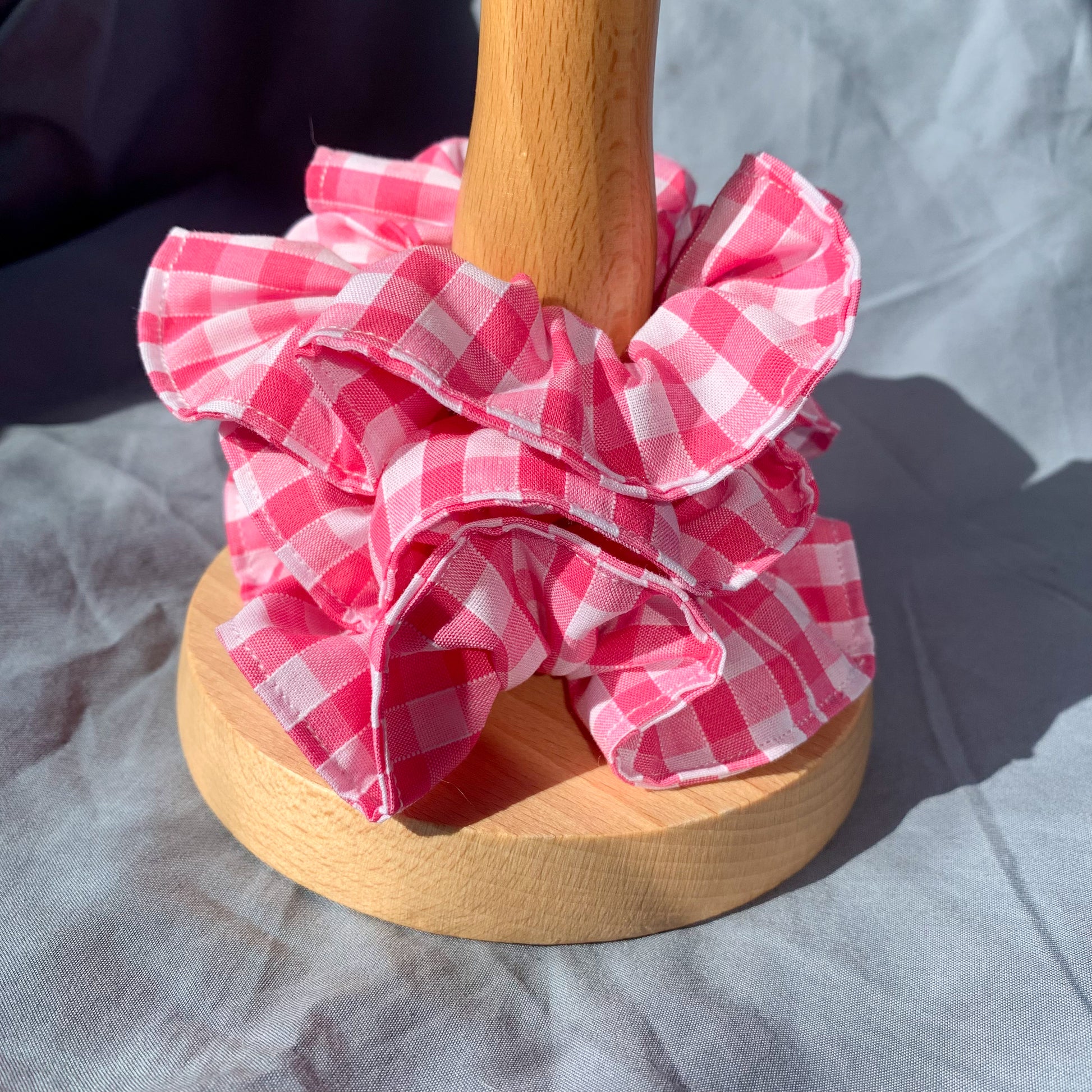 A stack of three pink gingham scrunchies on a wooden pole against a blue background