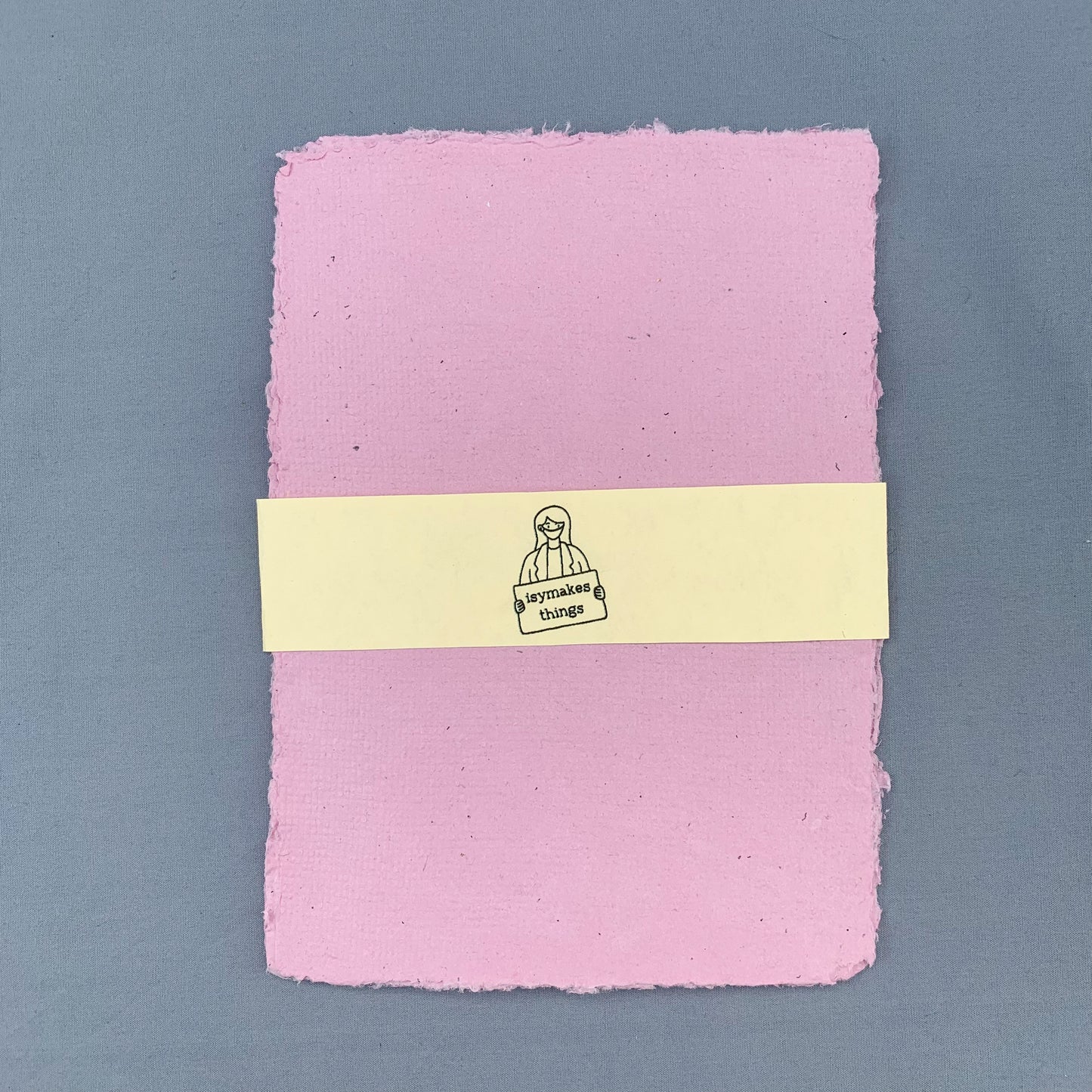 a stack of pink sheets of paper with a cream coloured isymakesthings logo sleeve around them against a blue background