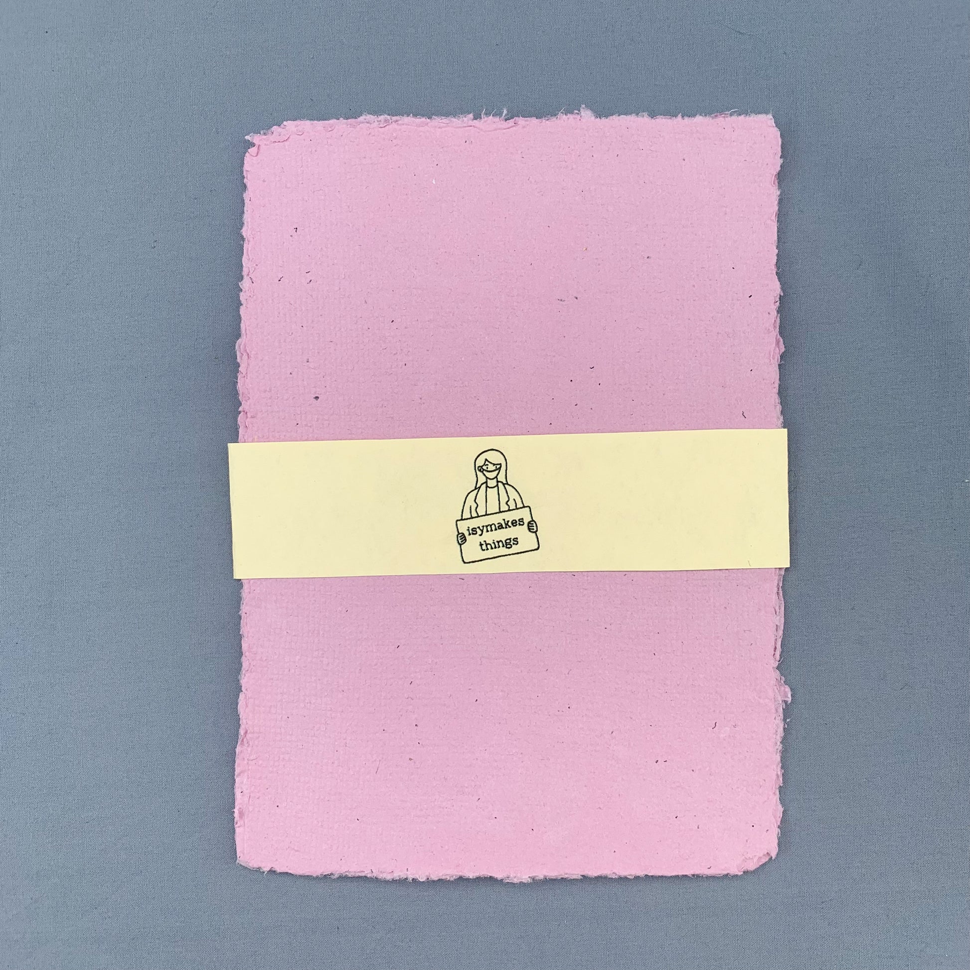 a stack of pink sheets of paper with a cream coloured isymakesthings logo sleeve around them against a blue background