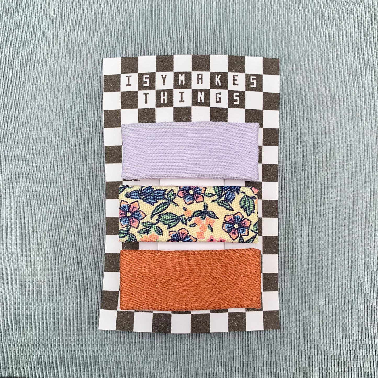 three pink & purple floral print rectangle hair clips on a checkerboard backing card with the title "isymakesthings" against a blue grey background