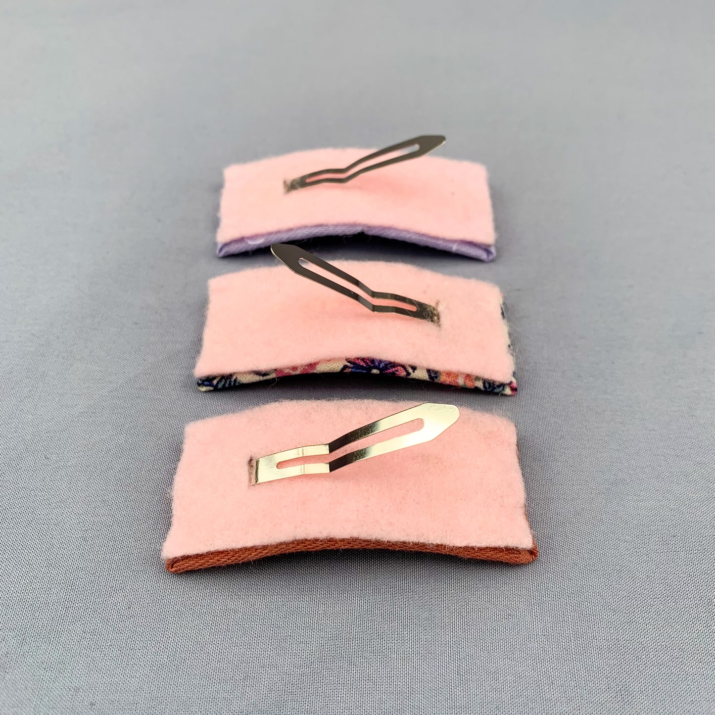 the underside of three pink hair clips with their metal prongs in the air on a grey blue background